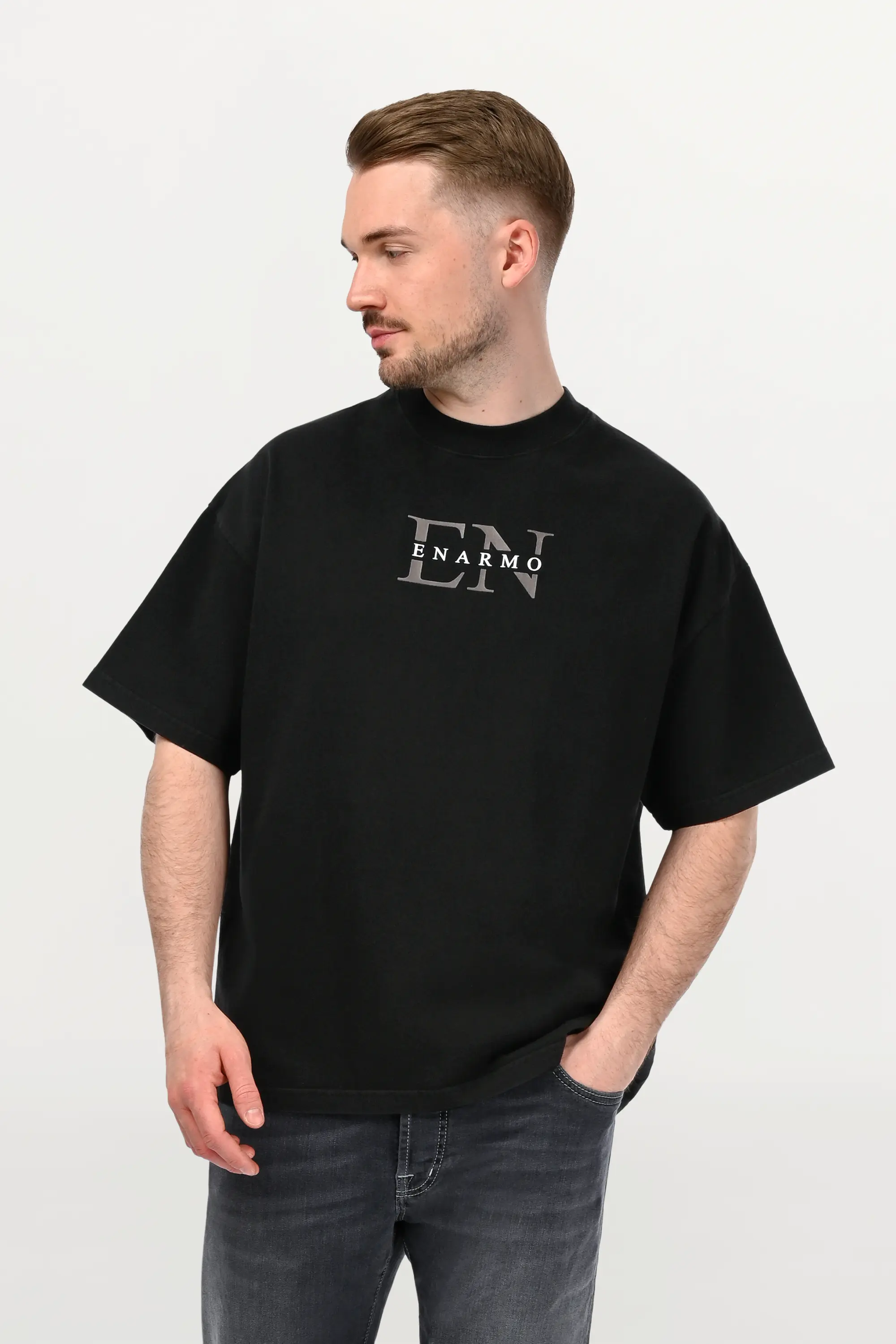 Close-up of black oversized ENARMO T-shirt featuring anthracite EN monogram with white logo detail on chest, worn by male model