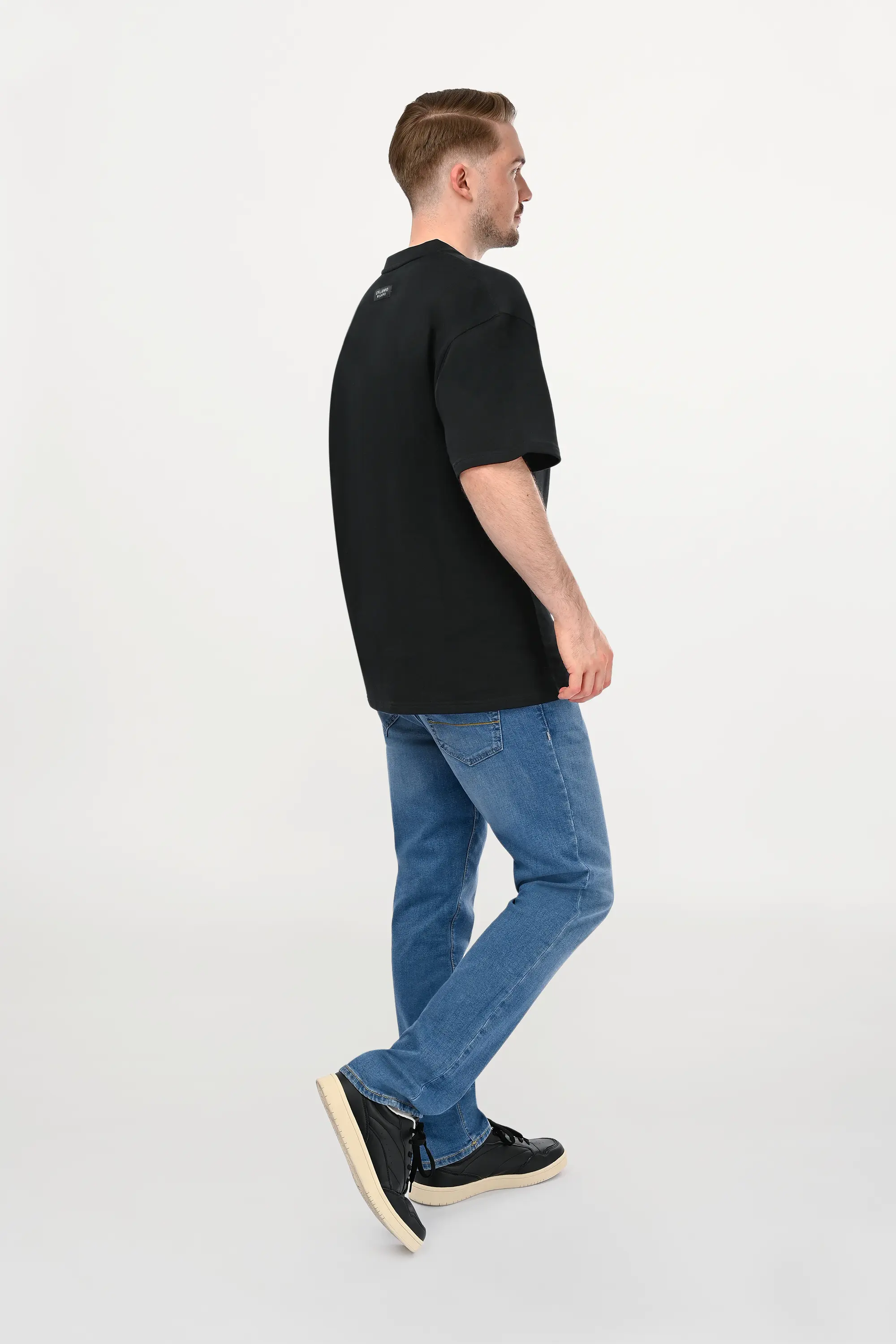 Side view of male model in black oversized luxury cotton T-shirt with sculpted silhouette and relaxed streetwear proportions