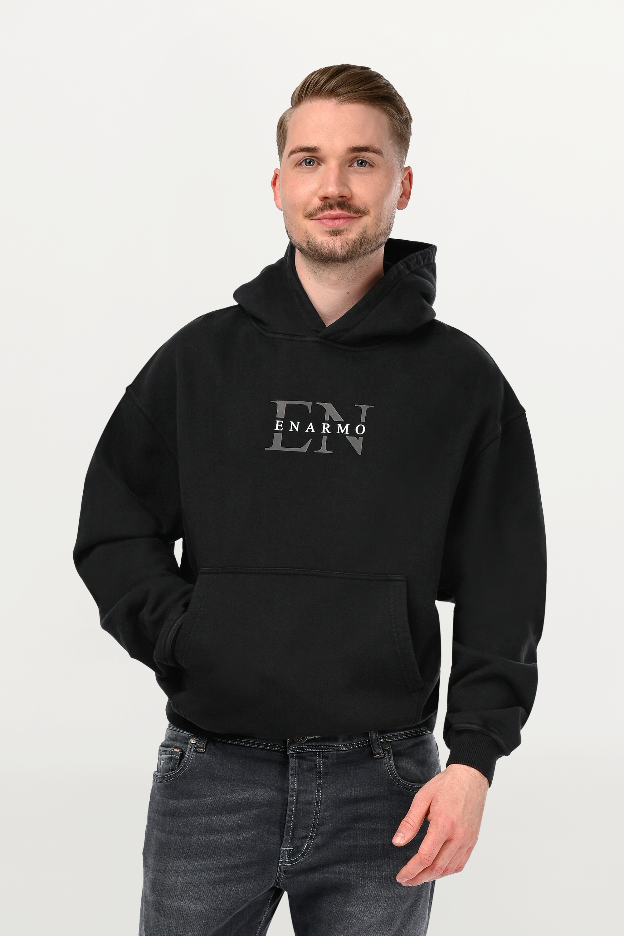 Close-up of EN Monogram on black oversized hoodie, detailed anthracite outline and subtle white ENARMO lettering on soft cotton fabric.