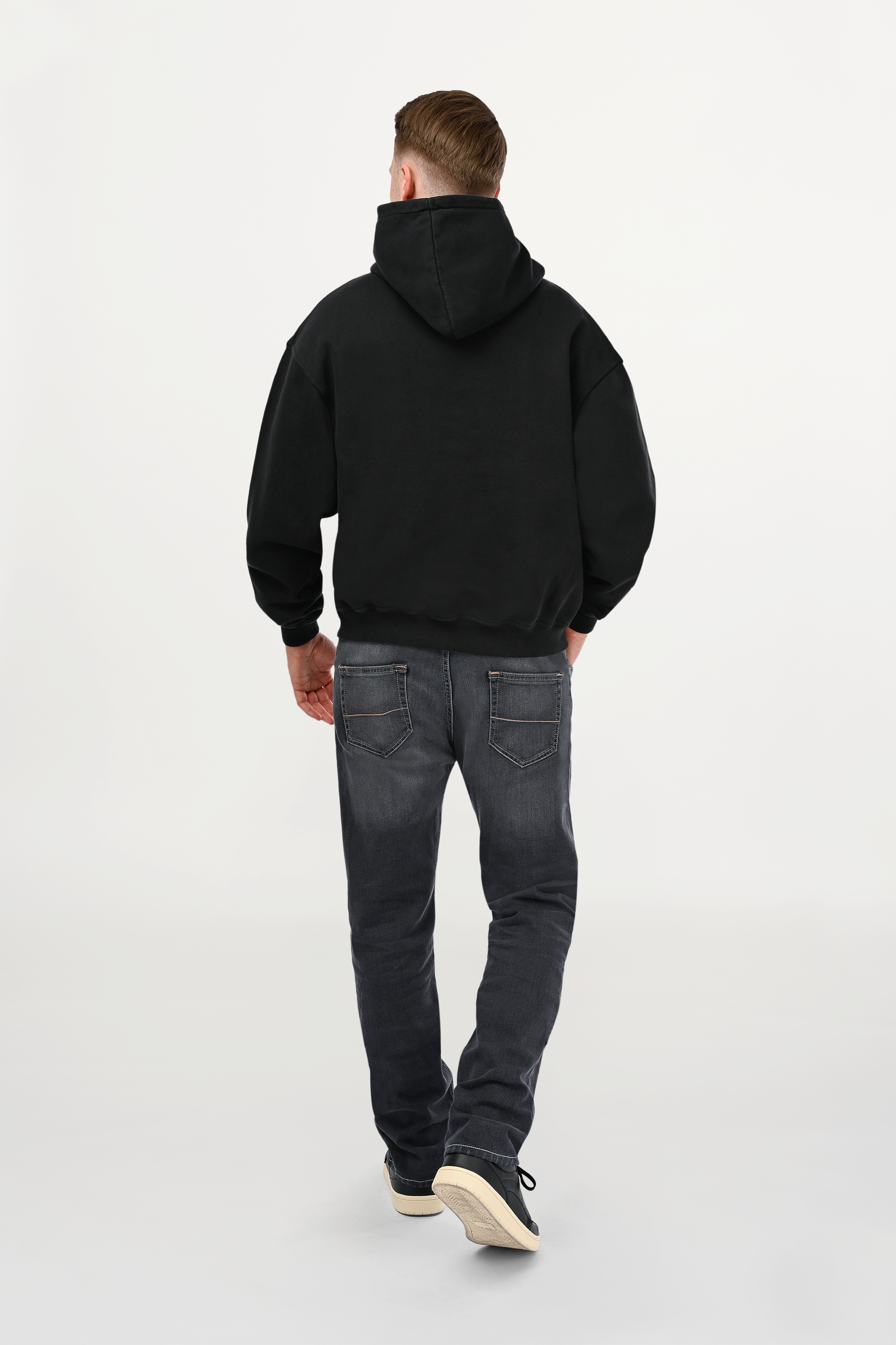 Rear view of male model in black oversized hoodie, smooth back panel, unisex fit, and elevated contemporary street-luxury design.