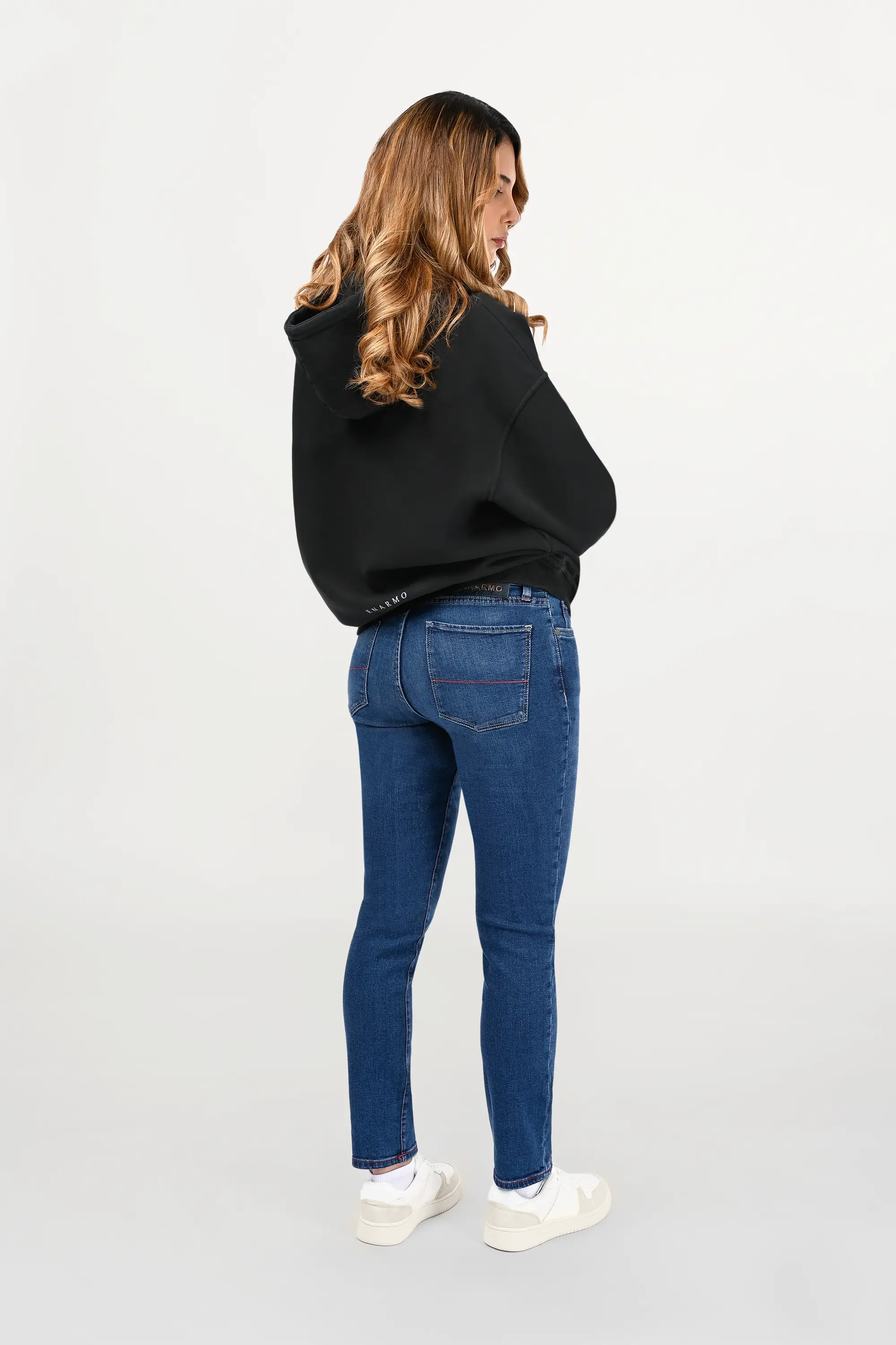 Rear view of female model in black oversized hoodie, clean back panel with subtle sky-blue ENARMO signature placed at lower back.
