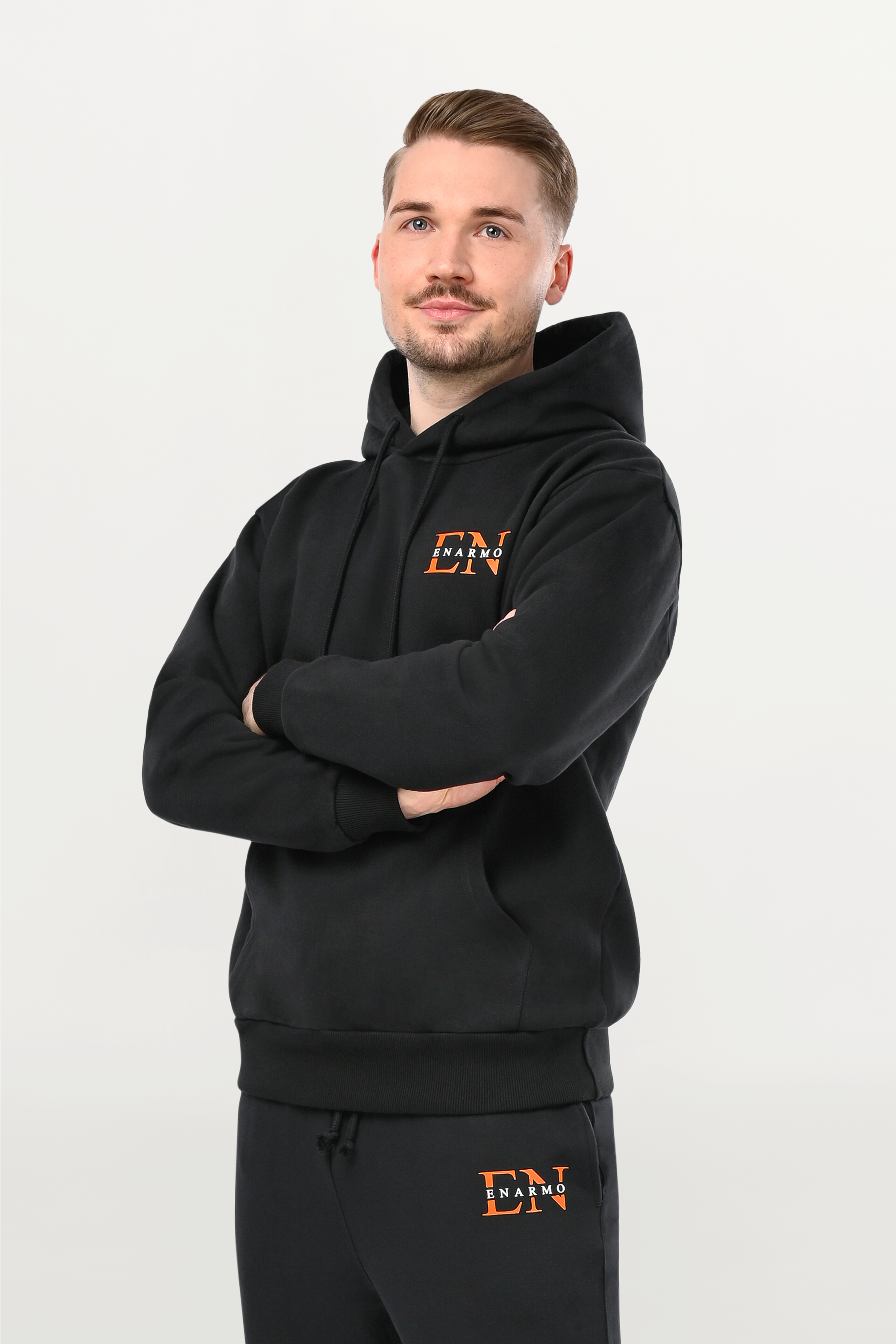 Angled close-up of orange EN monogram with white ENARMO lettering on black hoodie, detailed logo print on premium cotton fabric.