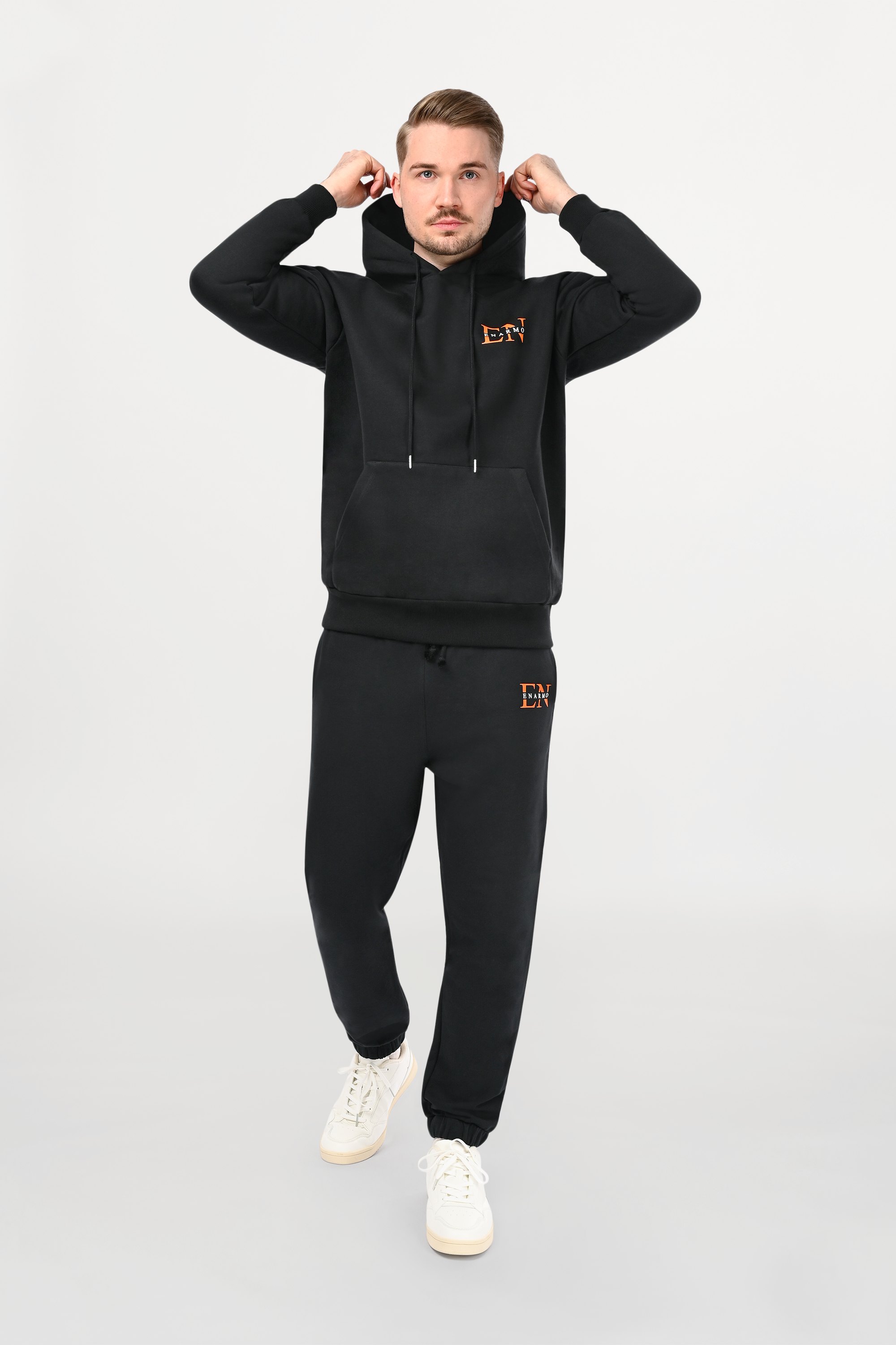 Male model wearing black cotton hoodie with orange and white EN monogram on left chest, regular fit silhouette and modern designer styling.