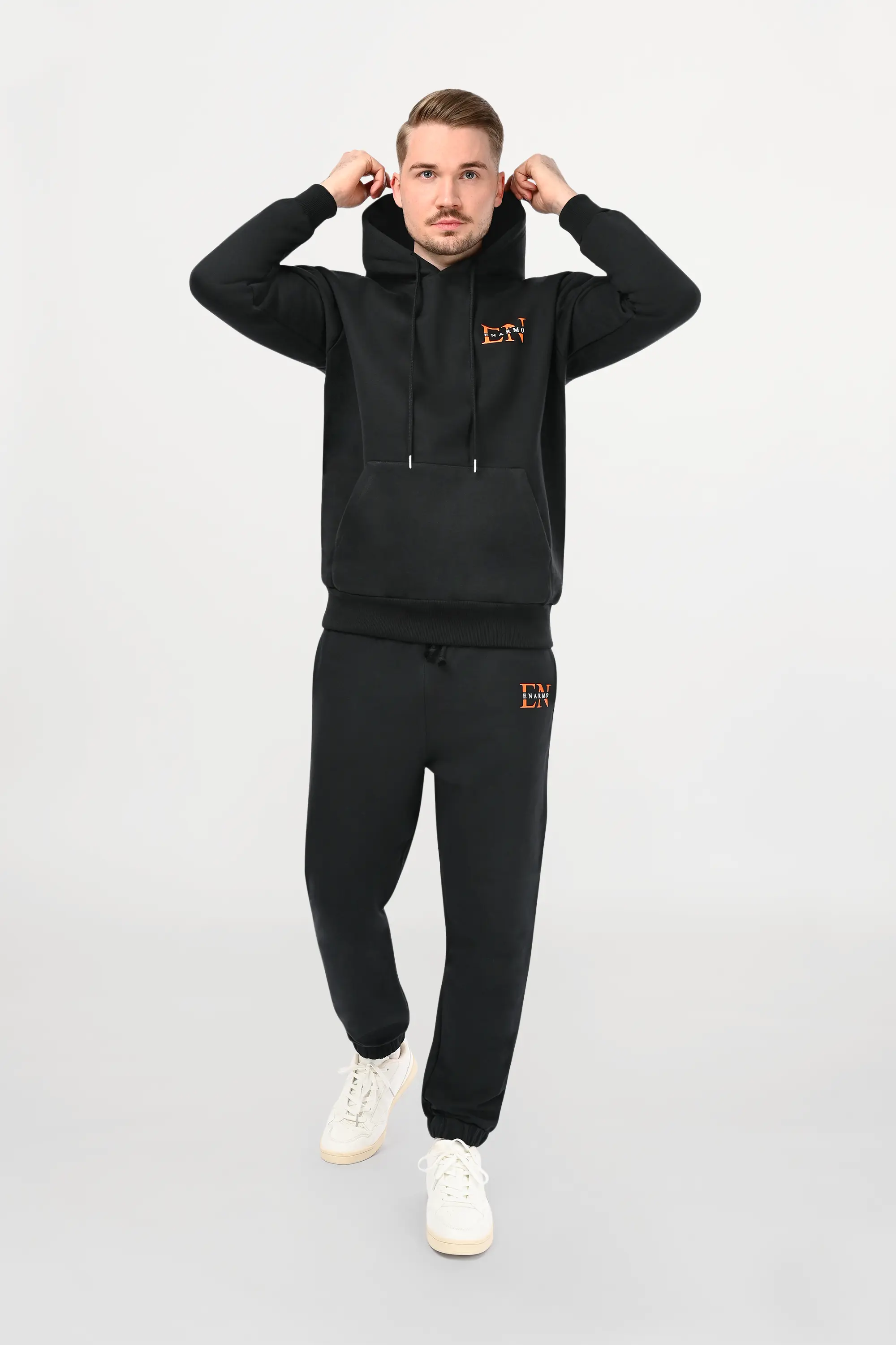 Male model wearing black cotton hoodie with orange and white EN monogram on left chest, regular fit silhouette and modern designer styling.