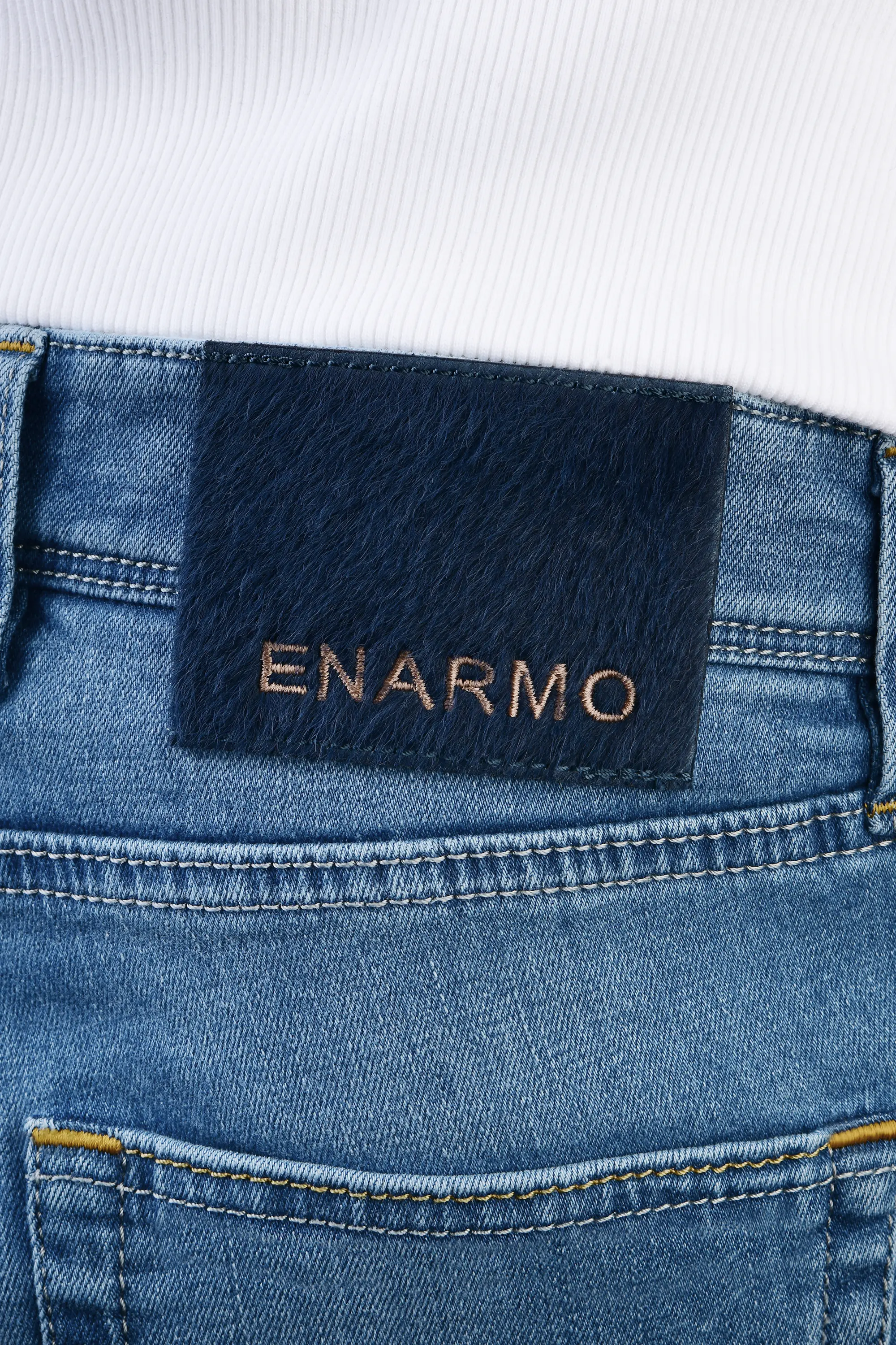 Close-up of rear waistband on light blue jeans showing pony hair patch with ENARMO embroidery and premium craftsmanship detail.