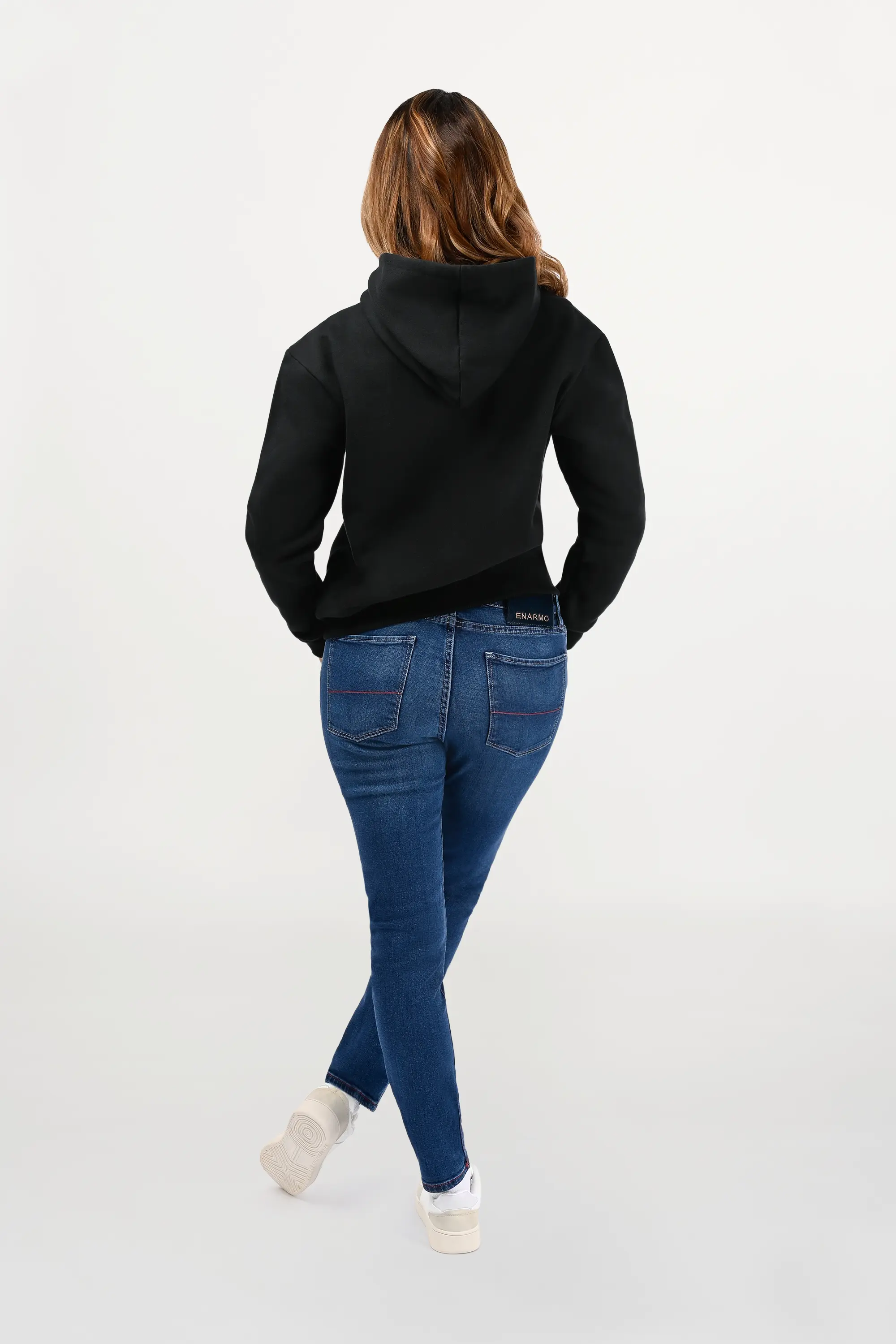 Back view of female model wearing a mid blue skinny jeans, showing clean back pockets, slim fit contour, and subtle fading for refined luxury look.