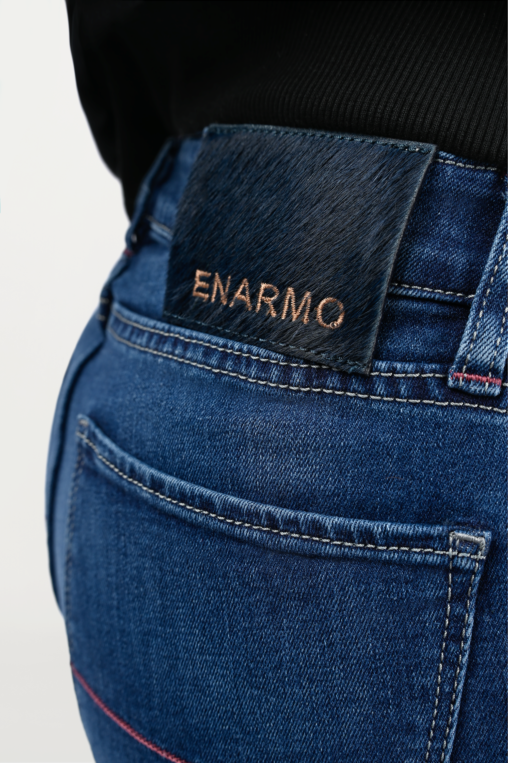 Rear view close-up of pony hair patch with ENARMO embroidery on waistband, mid blue skinny jeans worn by female model, emphasizing luxury detailing.