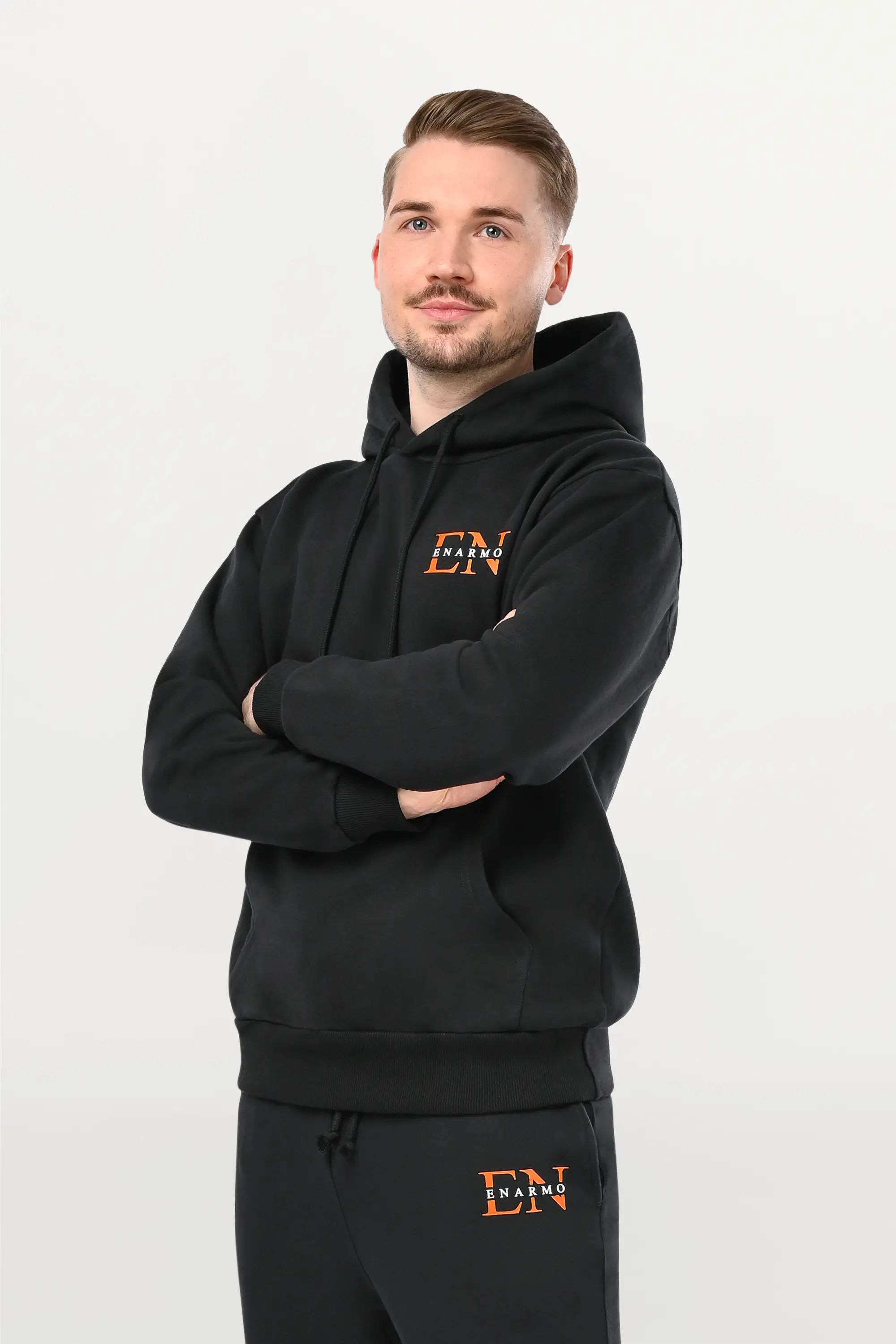 Angled close-up of orange EN monogram with white ENARMO lettering on black hoodie, detailed logo print on premium cotton fabric.