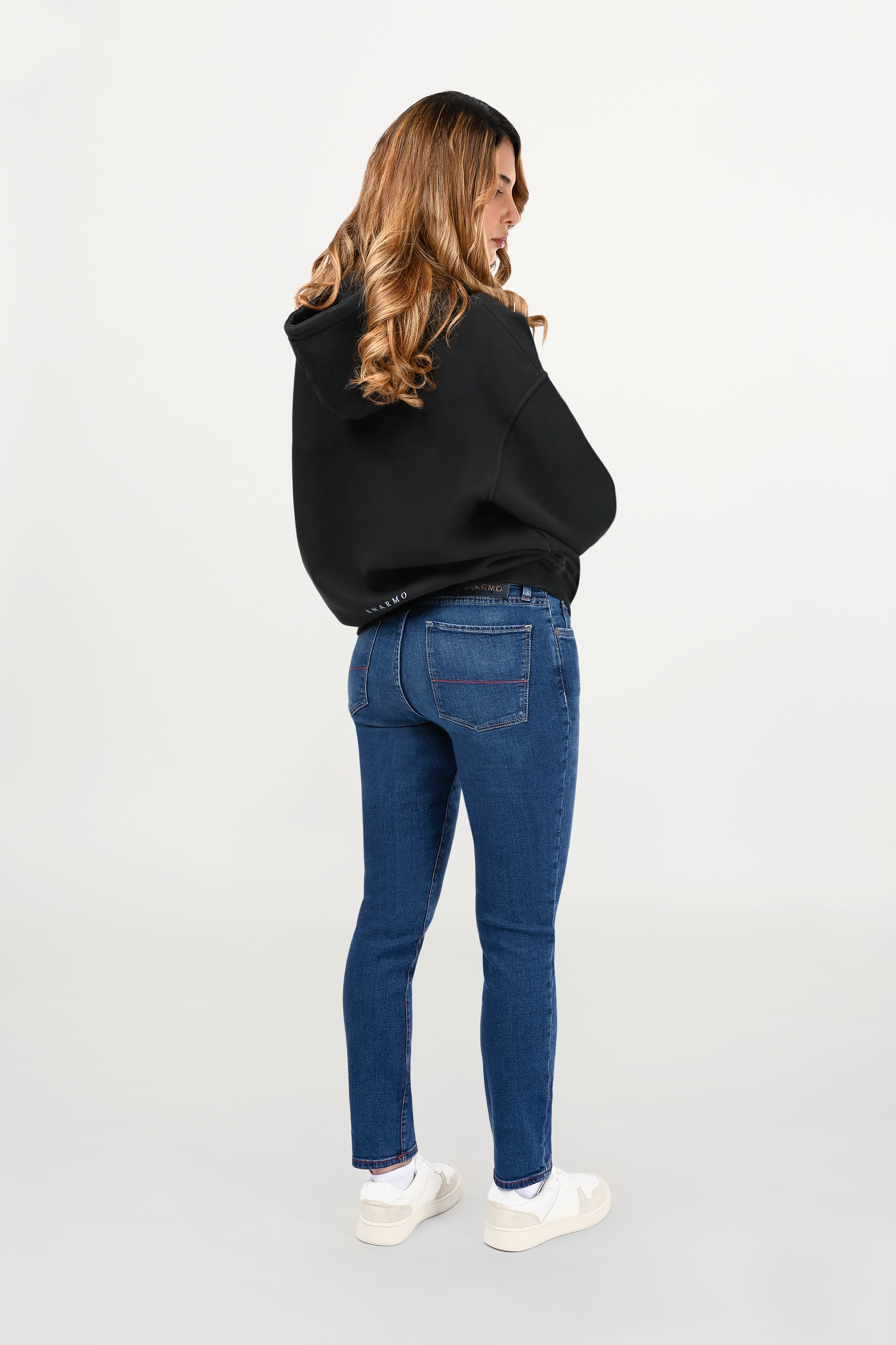 Rear view of female model in black oversized hoodie, clean back panel with subtle sky-blue ENARMO signature placed at lower back.