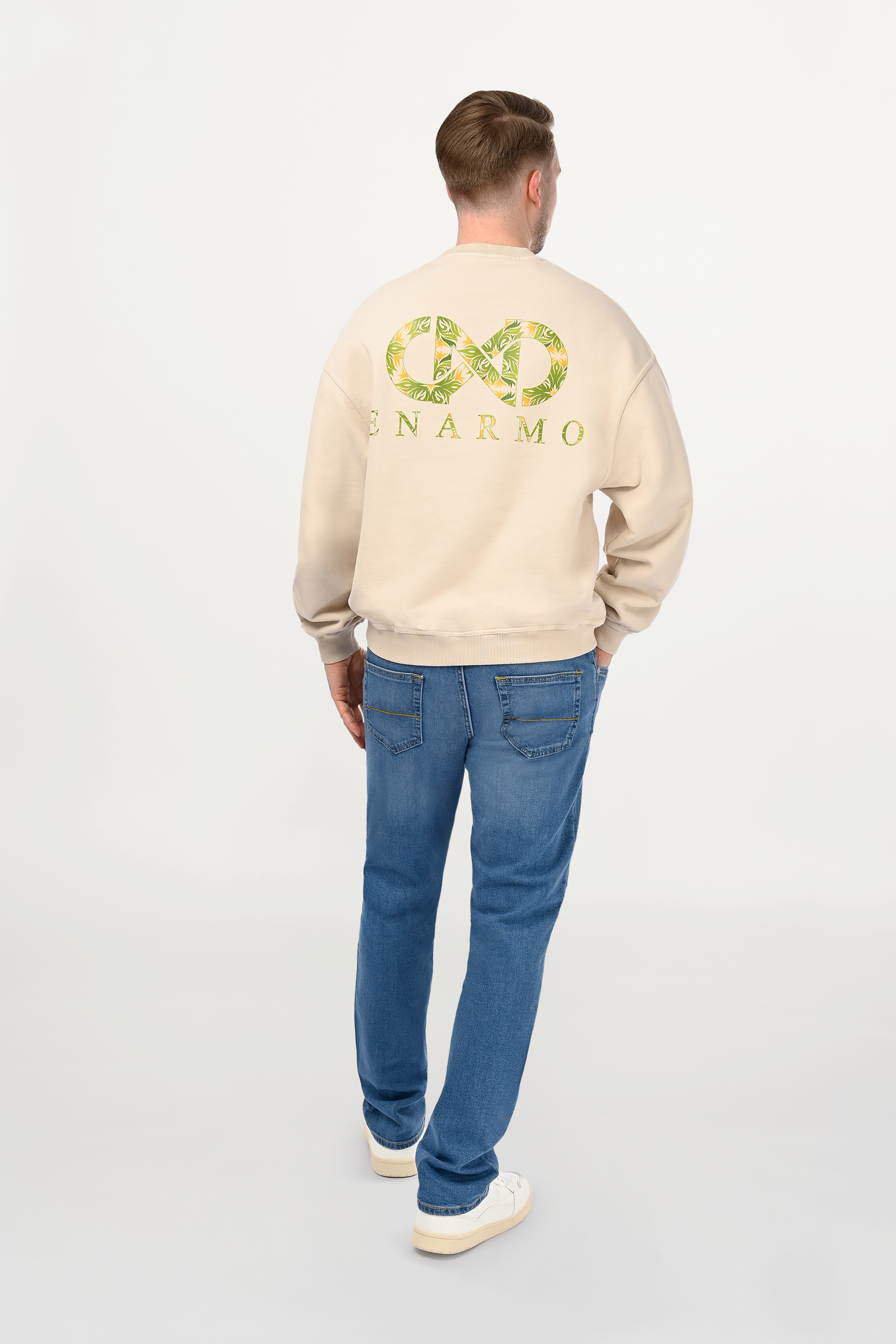 Rear view of male model in beige oversized sweatshirt featuring large yellow and green logo back print, contemporary street-luxury aesthetic.