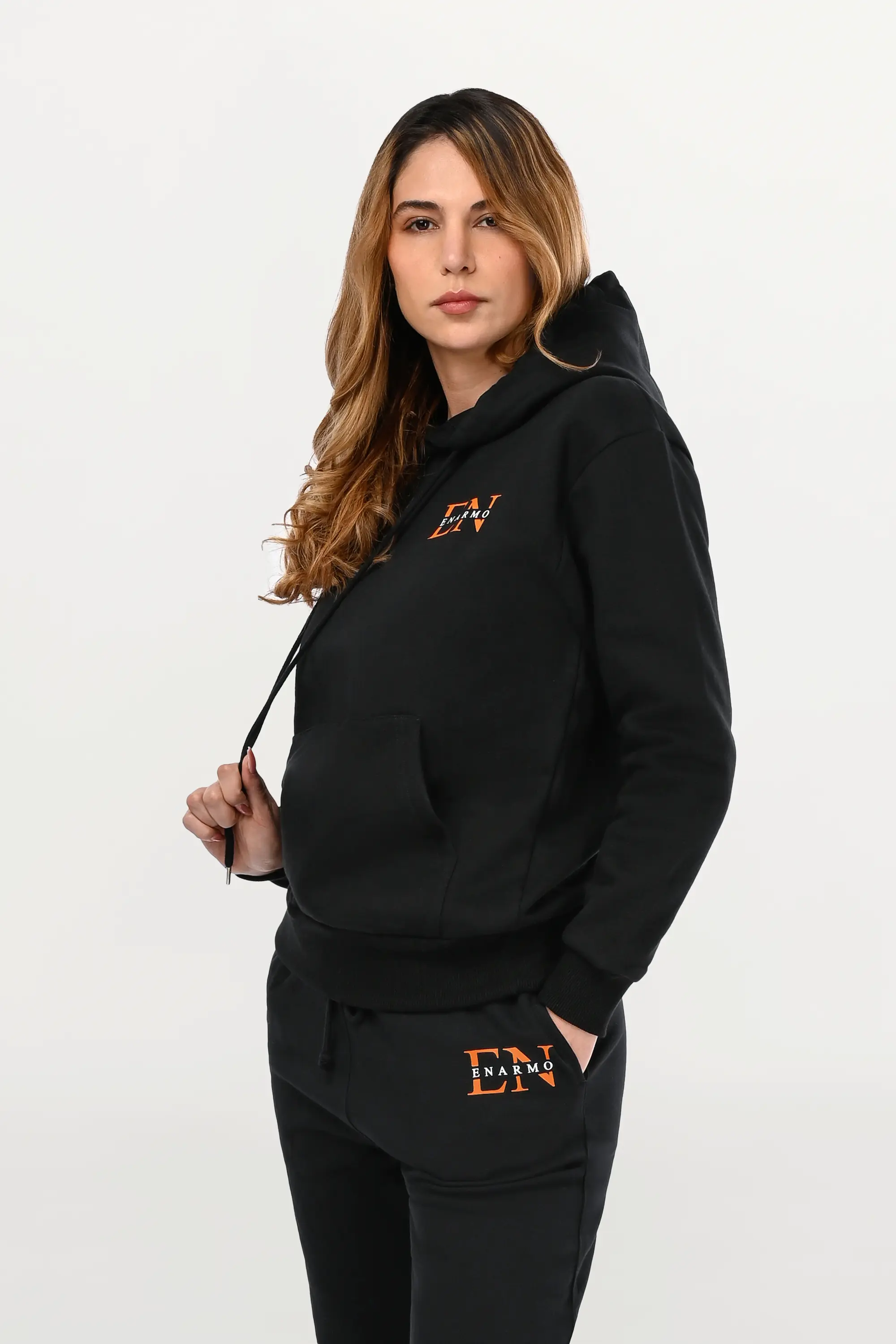 Close-up angled view of chest monogram on black hoodie, orange EN outline with white ENARMO signature on soft cotton material.