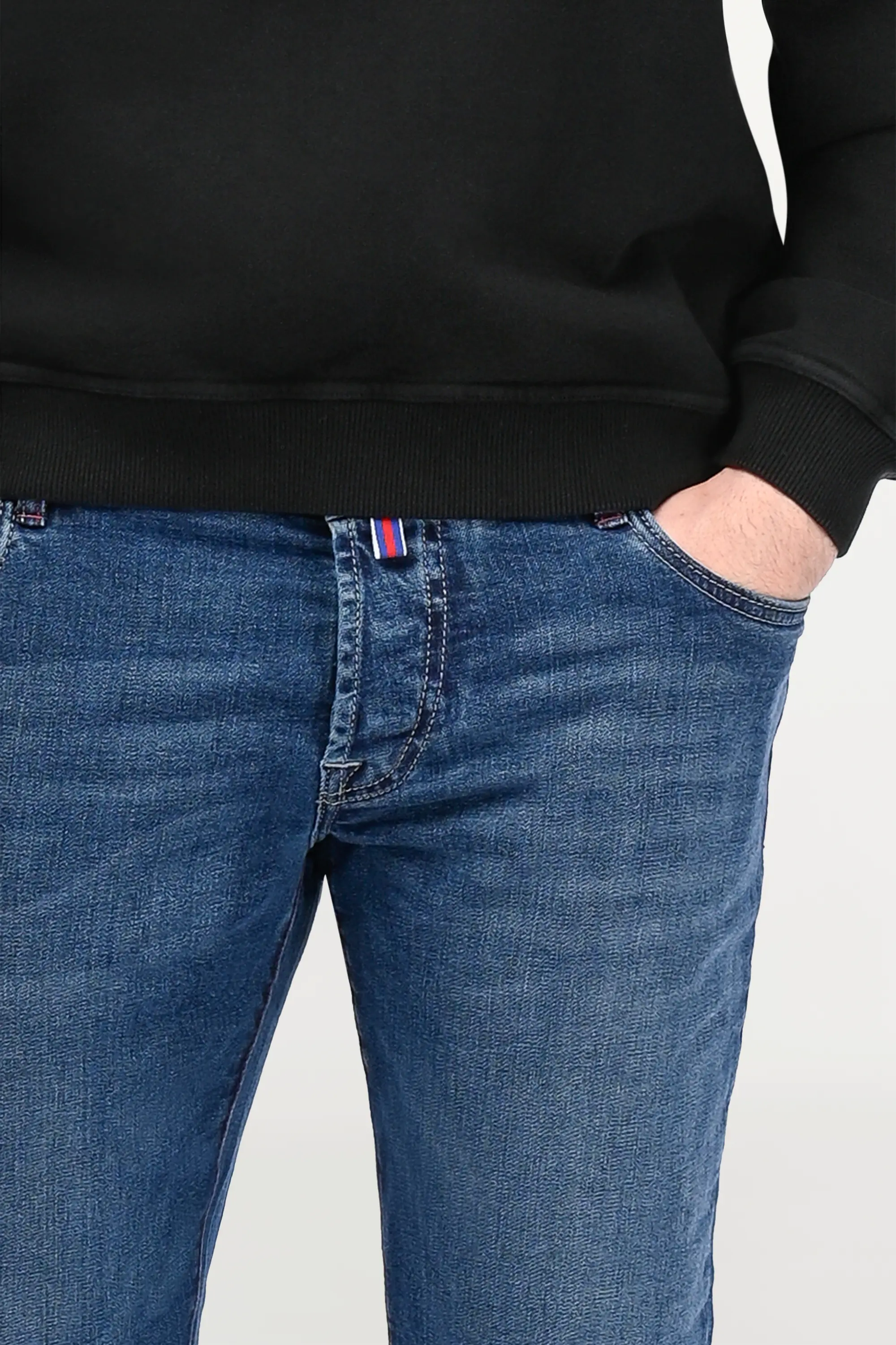Close-up of mid blue stretch denim jeans showing refined fading, premium cotton blend fabric and tailored fit structure.