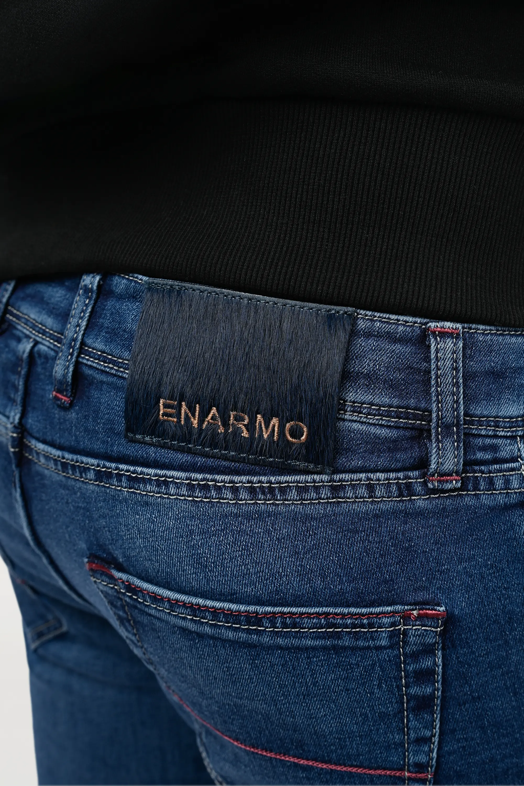 Close-up of side back waist on mid blue denim jeans showing pony hair patch with ENARMO embroidery