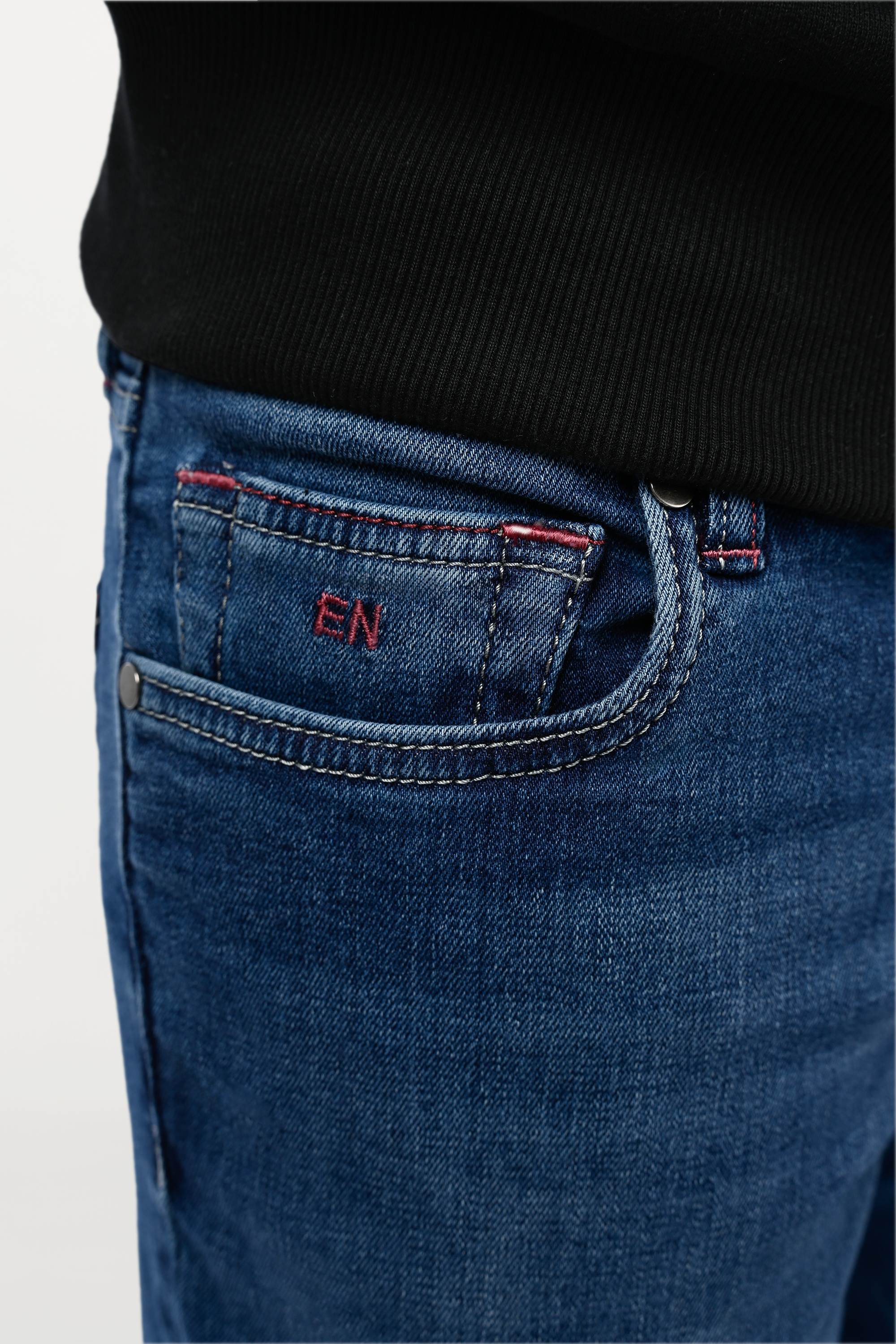 Detailed view of coin pocket on mid blue denim jeans featuring embroidered EN monogram, signature luxury detail on classic five-pocket design.