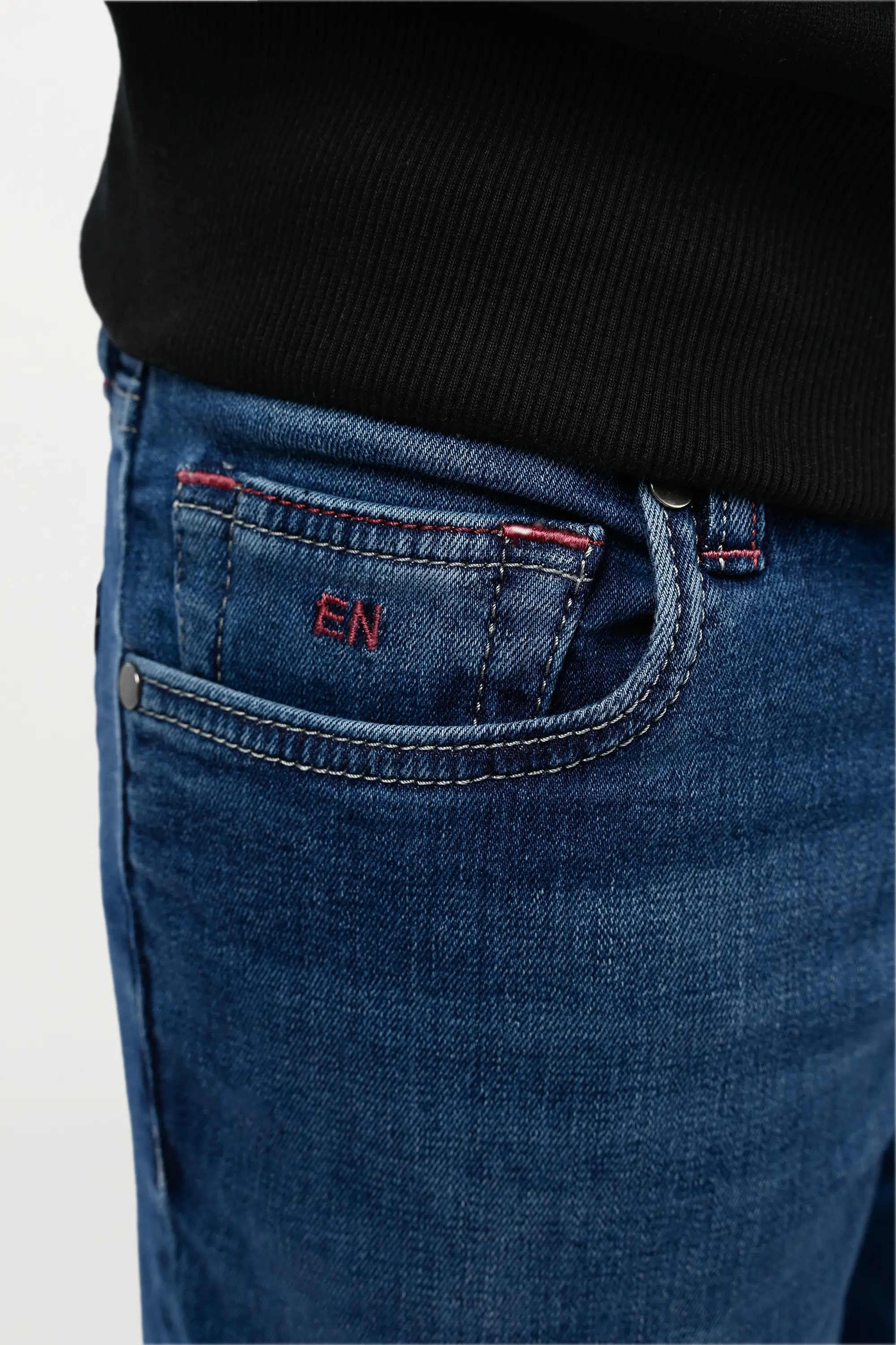 Detailed view of coin pocket on mid blue denim jeans featuring embroidered EN monogram, signature luxury detail on classic five-pocket design.