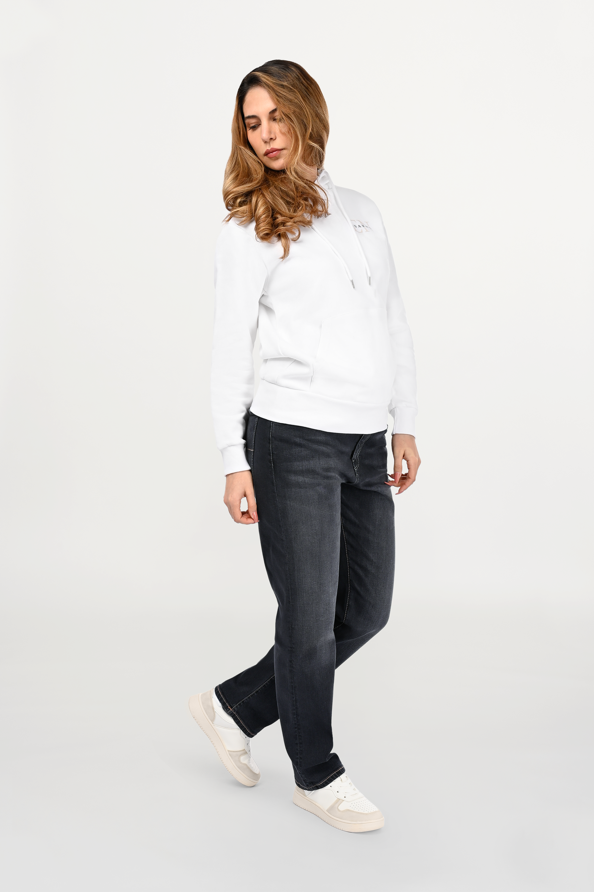 Female model wearing white cotton hoodie with beige EN monogram and black ENARMO signature on left chest, regular fit silhouette shown from angled front view.