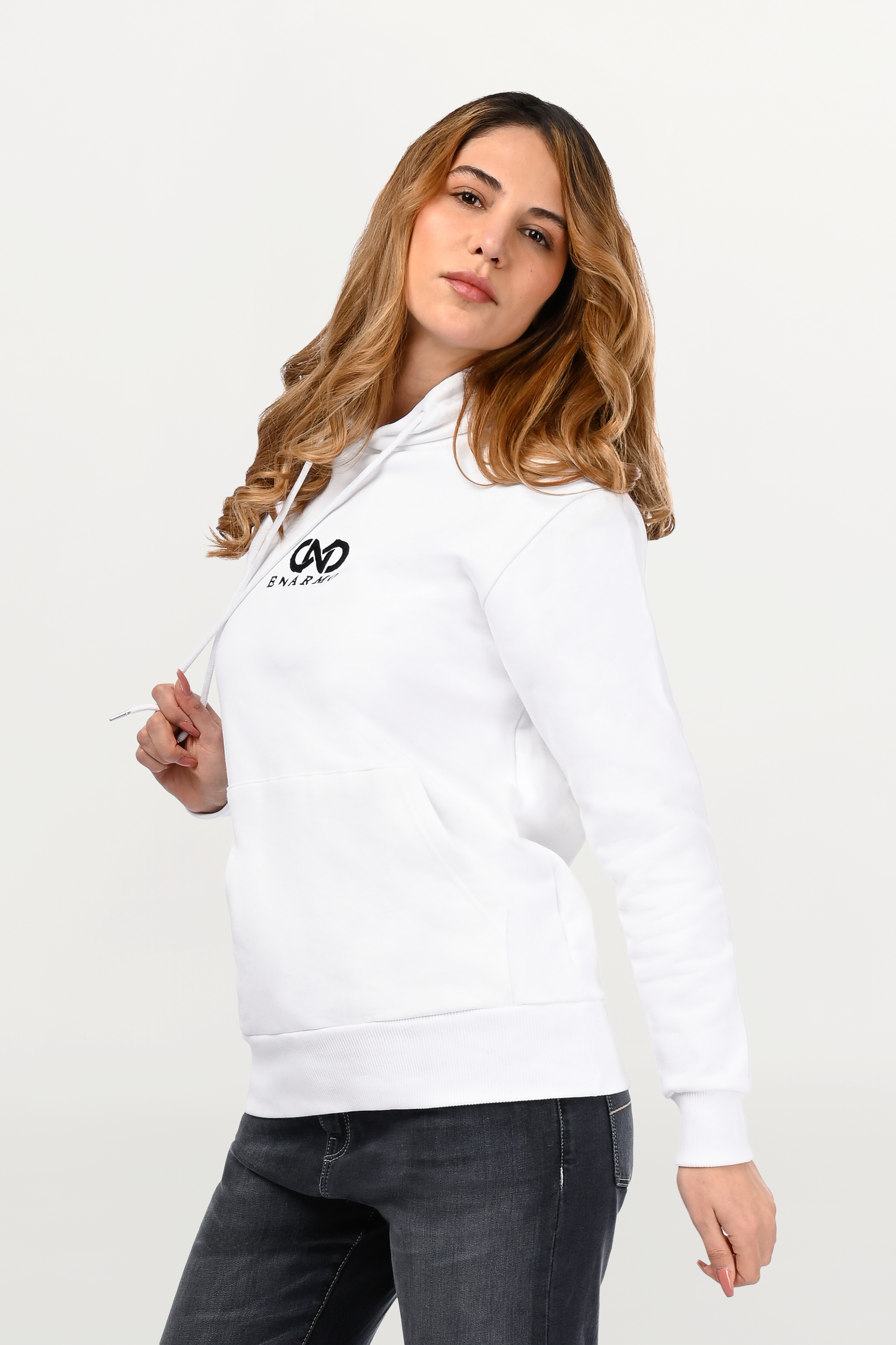 Close-up angled view of black embroidered ENARMO logo on white cotton hoodie, detailed stitching on bright fabric surface.