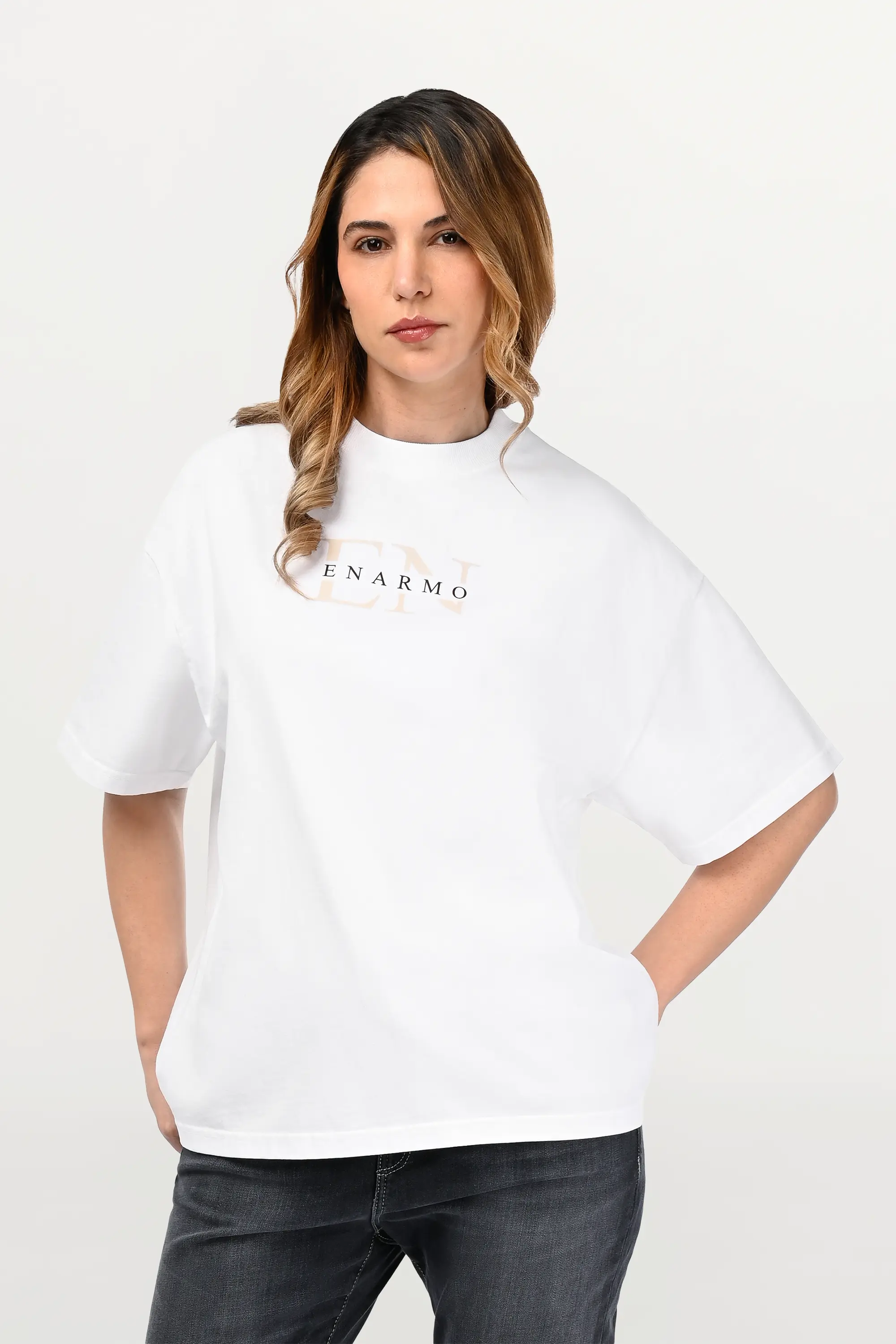 Close-up of white oversized ENARMO T-shirt showing beige EN monogram with black logo detail on chest, worn by female model