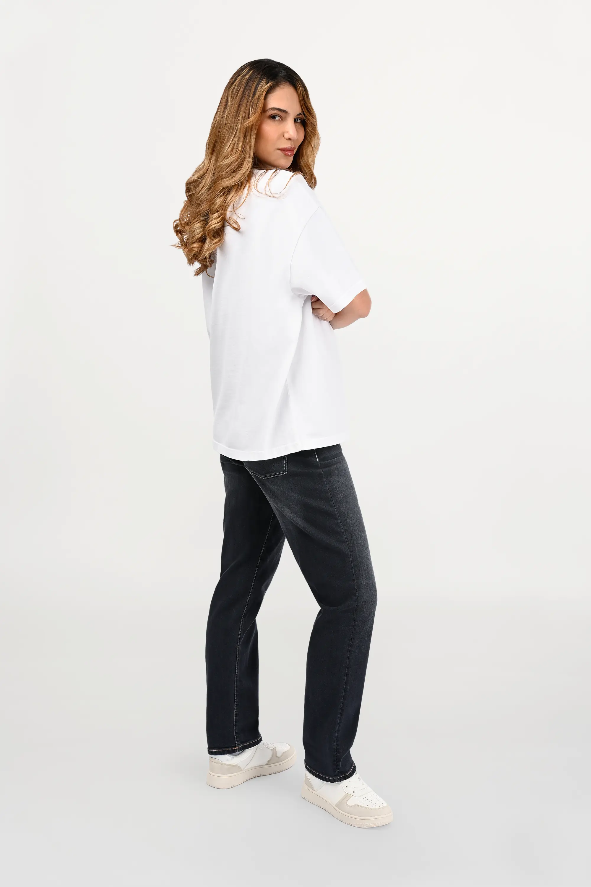 Side view of female model wearing white oversized cotton ENARMO T-shirt with beige EN monogram print, modern luxury streetwear silhouette