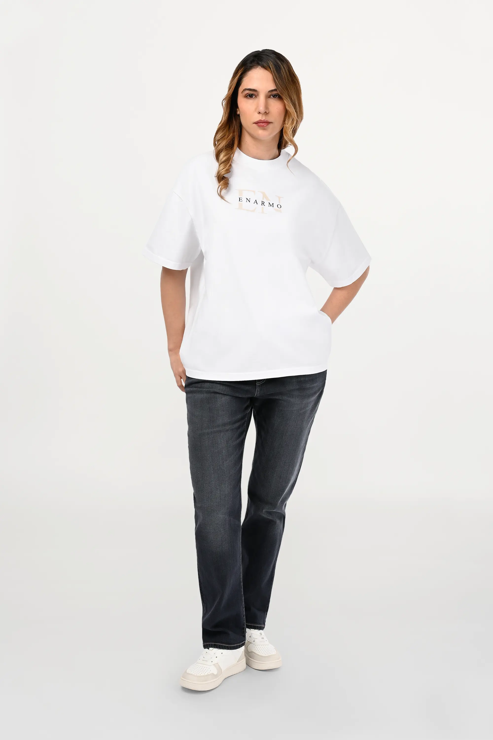 White oversized cotton T-shirt with beige EN monogram and black ENARMO logo worn by female model, relaxed luxury streetwear front view