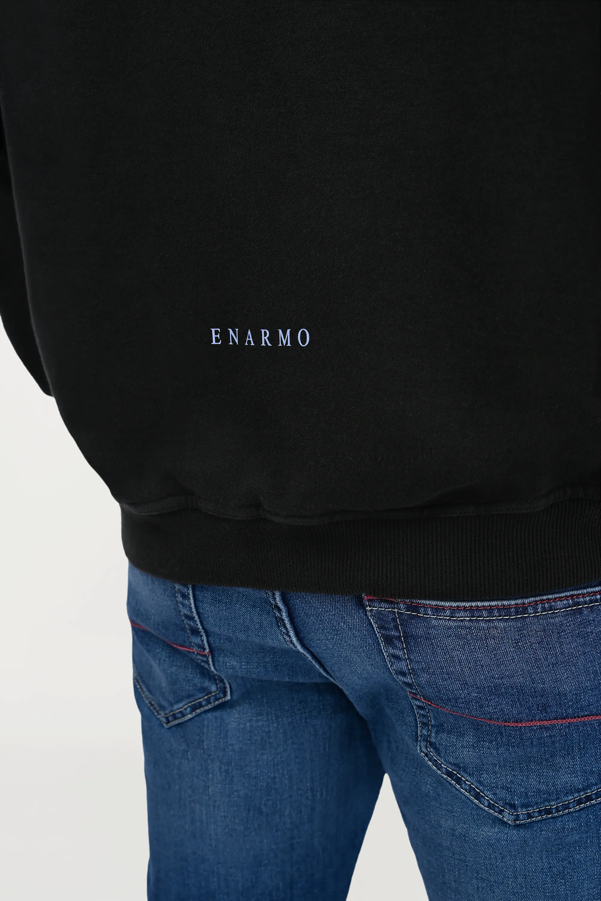 Close-up of small sky blue ENARMO print on lower back of black oversized hoodie, minimal branding detail on cotton fabric.