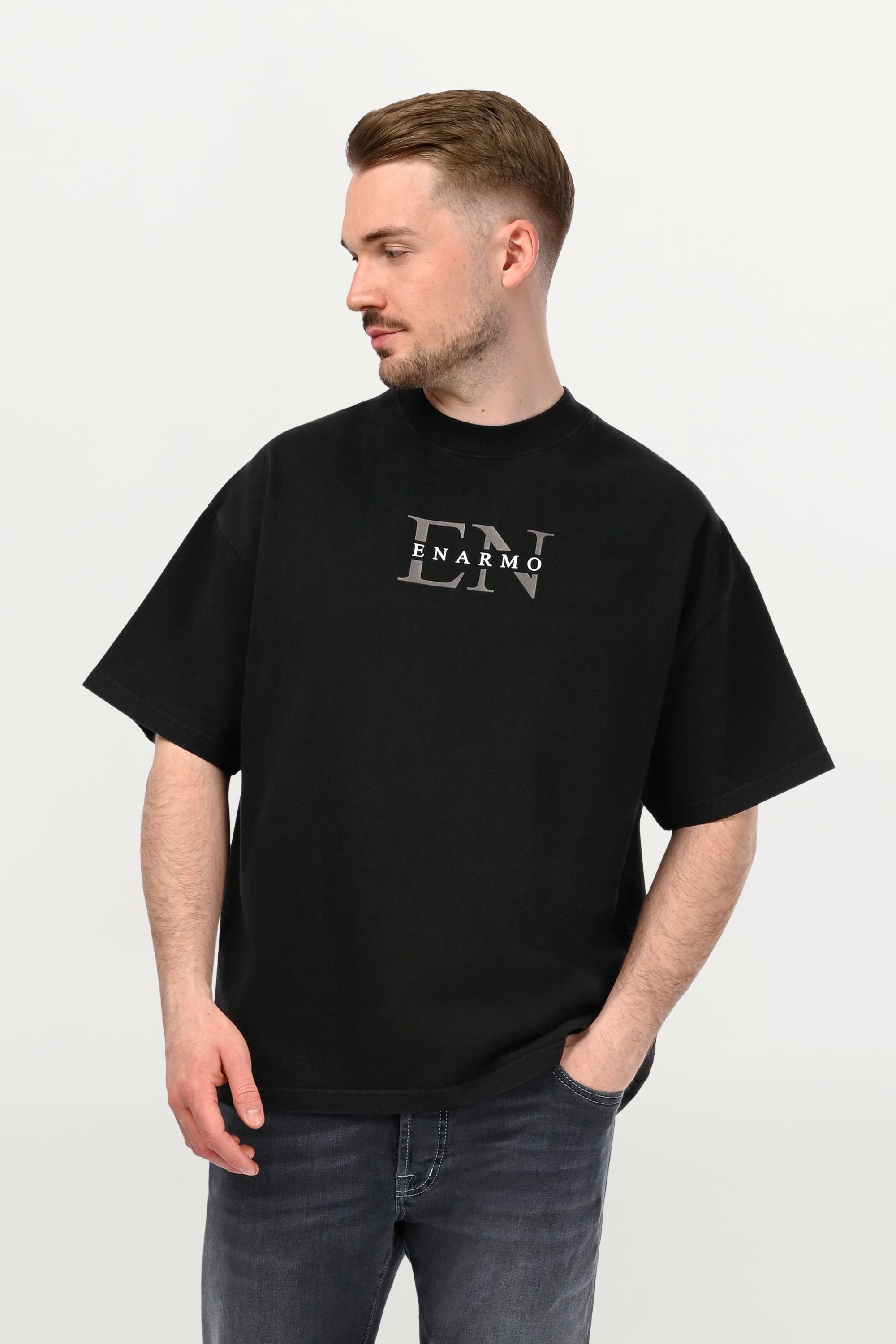 Close-up of black oversized ENARMO T-shirt featuring anthracite EN monogram with white logo detail on chest, worn by male model