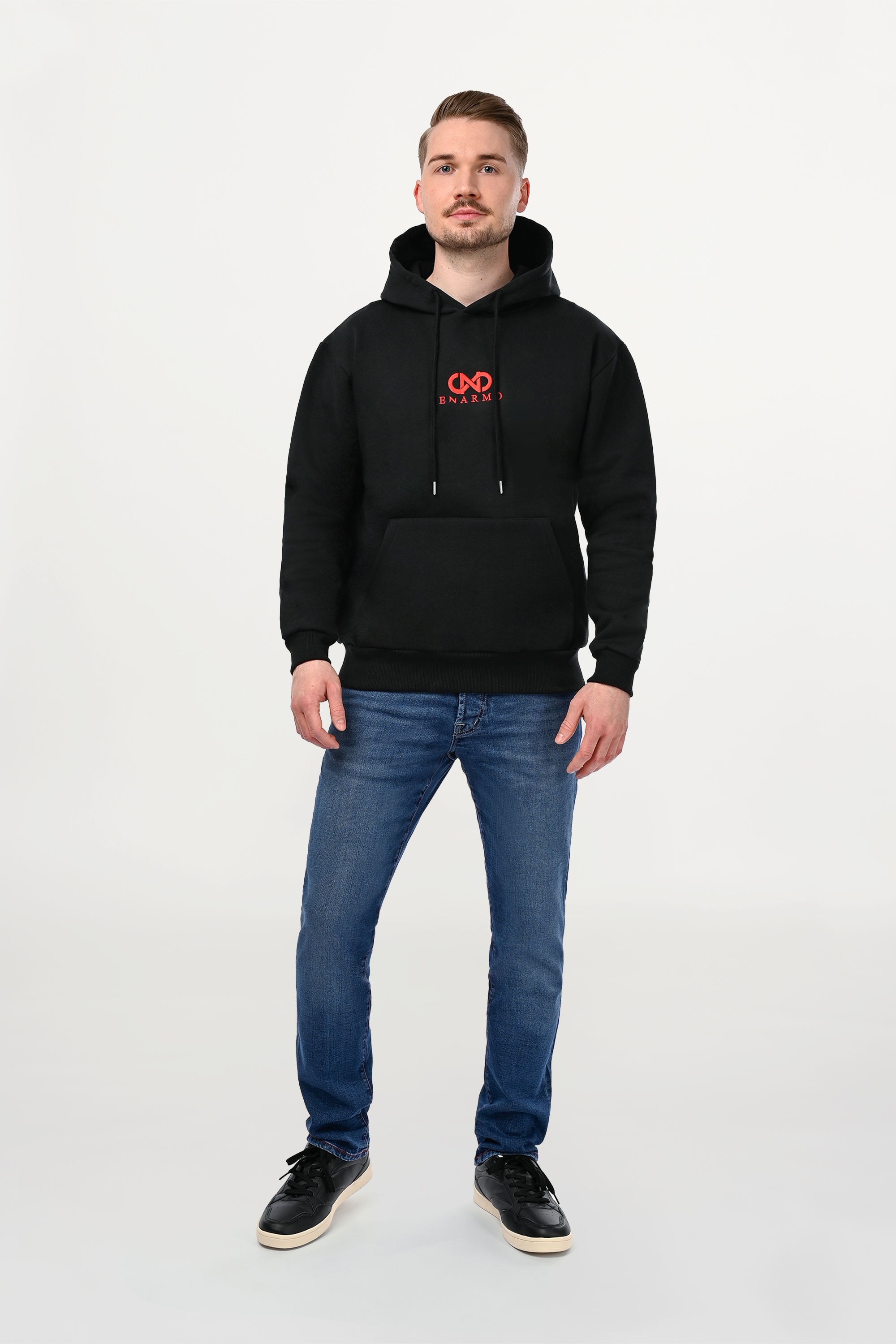 Male model wearing black cotton hoodie with central red ENARMO logo embroidery, regular fit silhouette