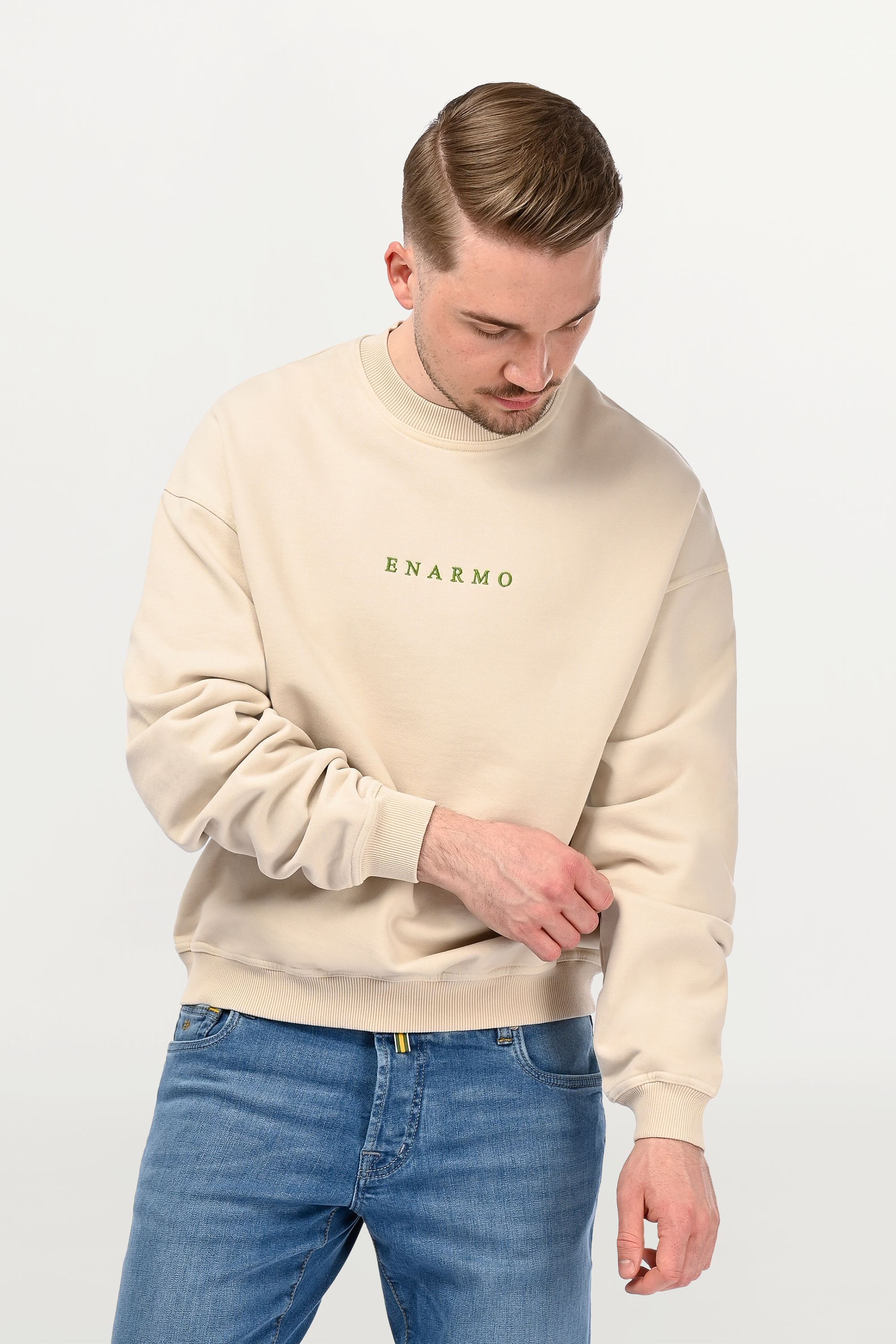 Close-up of green ENARMO embroidery on beige oversized crewneck, detailed stitching on soft cotton fabric with structured finish.