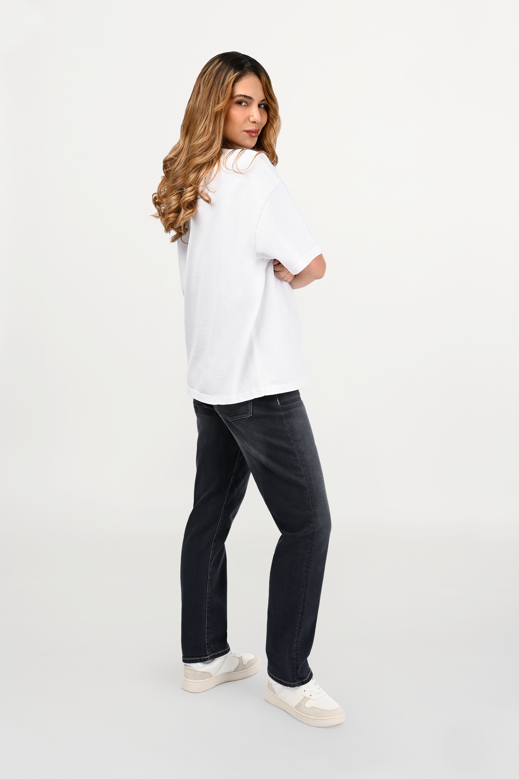 Side view of female model wearing white oversized cotton ENARMO T-shirt with beige EN monogram print, modern luxury streetwear silhouette