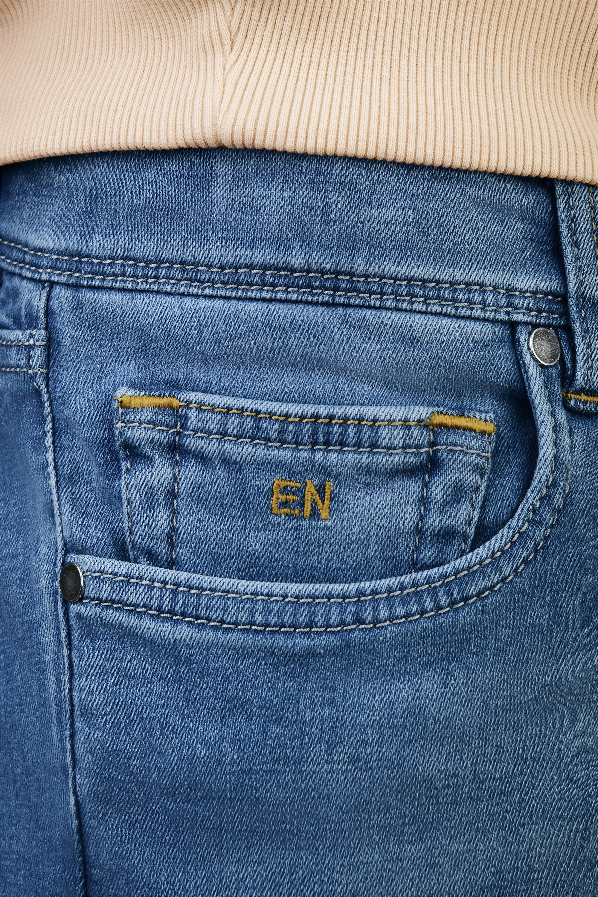 Close-up of coin pocket on light blue slim fit jeans featuring embroidered EN monogram canary yellow, signature detail on premium stretch denim.