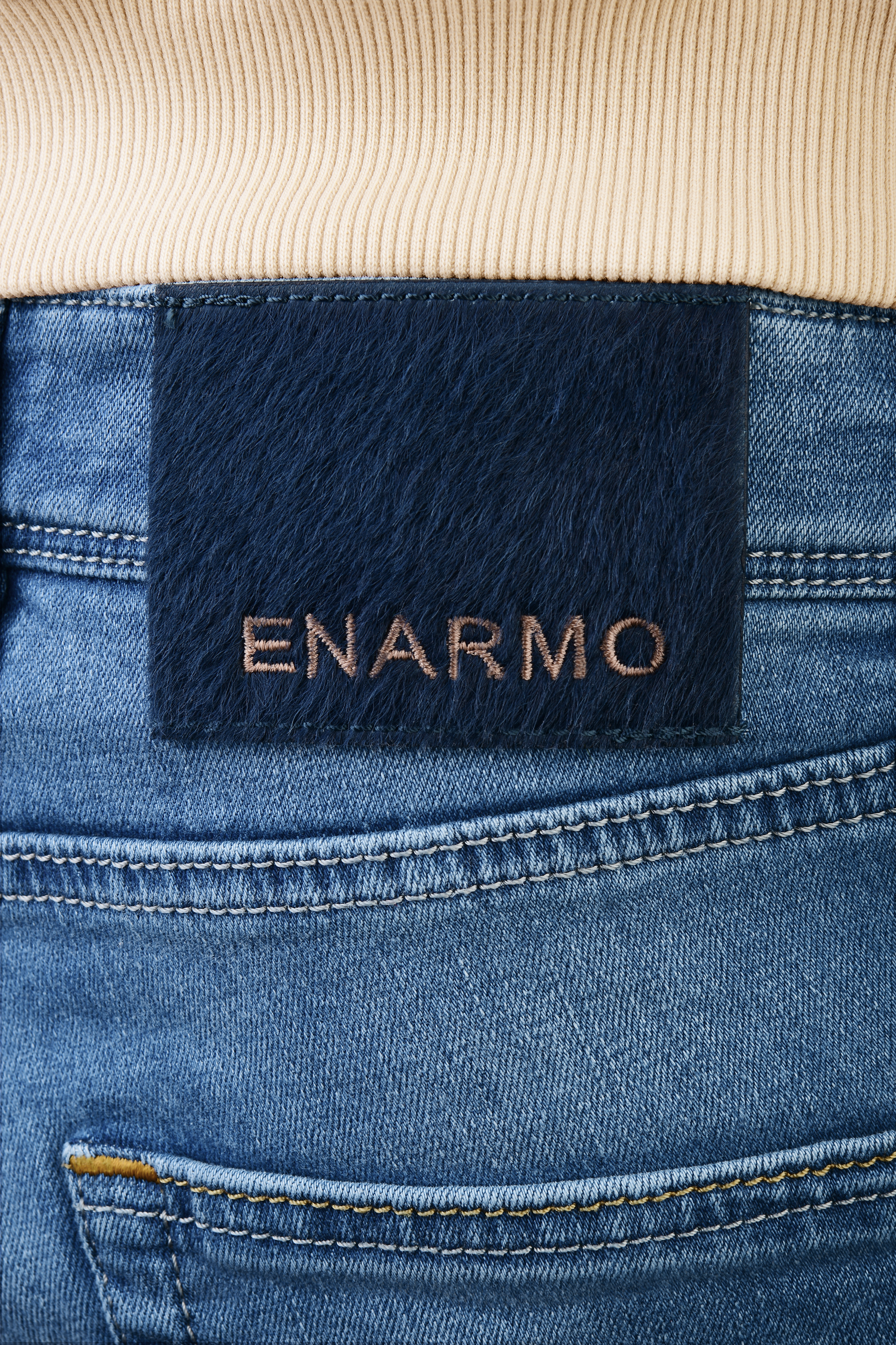 Detailed close-up of rear waistband showing pony hair patch with ENARMO embroidery on light blue designer denim jeans.