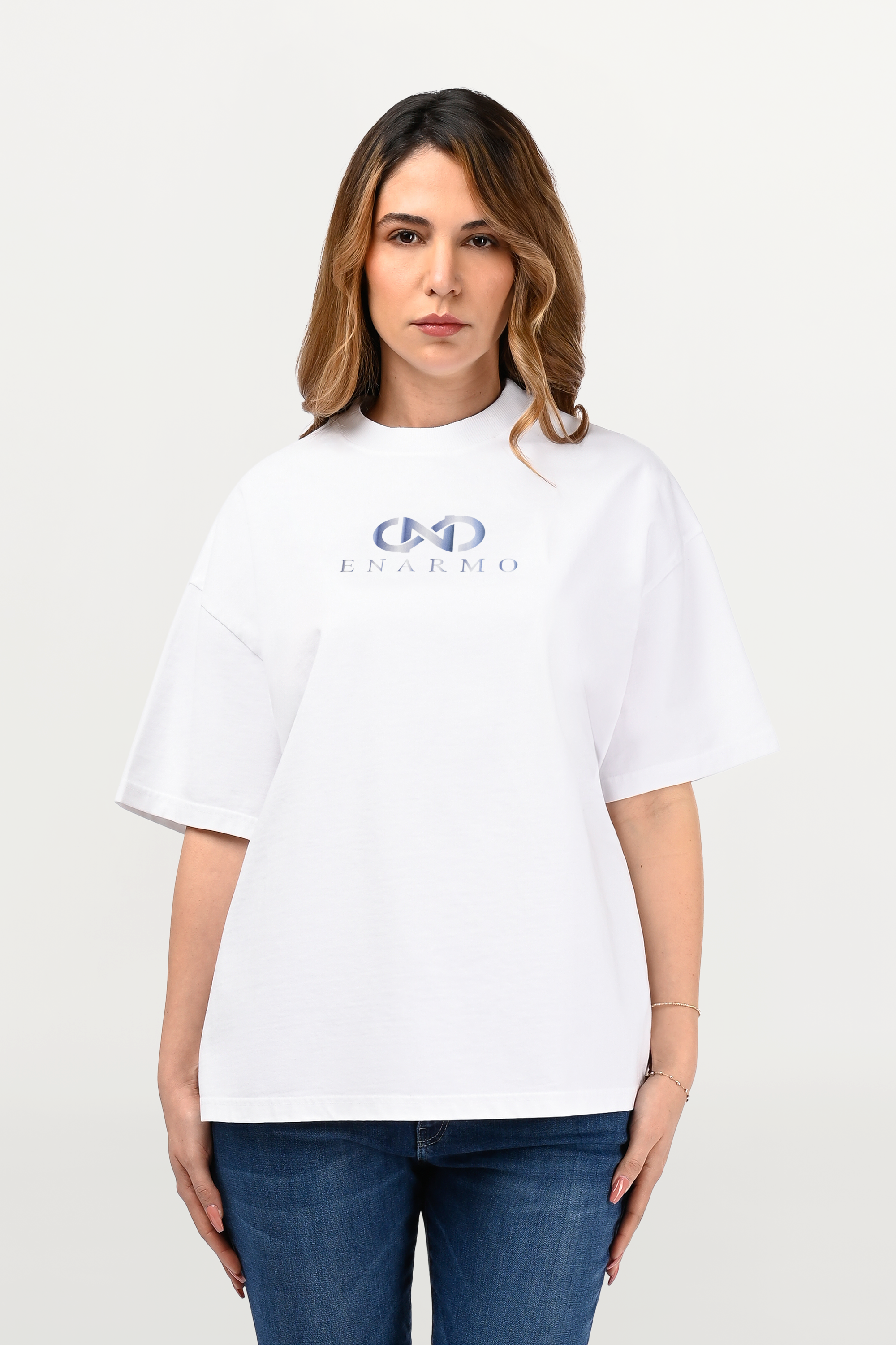 Close-up of sky-gradient chest logo on white oversized cotton T-shirt, highlighting premium fabric texture and refined ENARMO detailing, worn by female model.