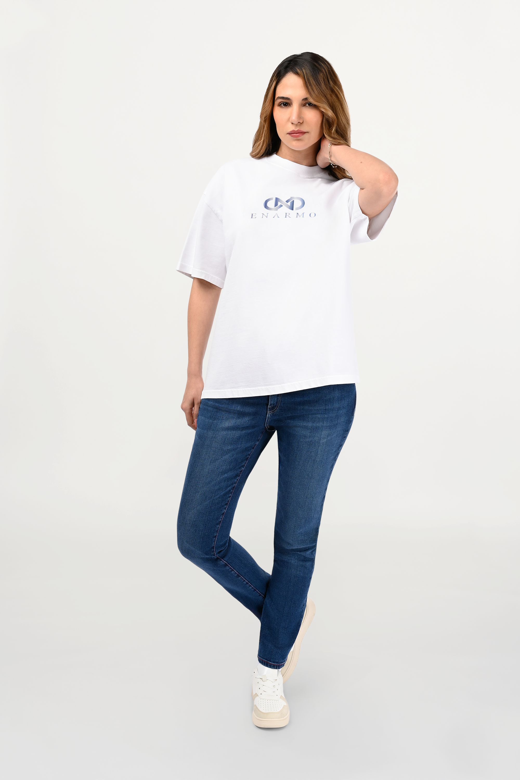Female model wearing white oversized cotton T-shirt with subtle sky-gradient logo on chest, relaxed unisex silhouette, contemporary luxury streetwear front view.