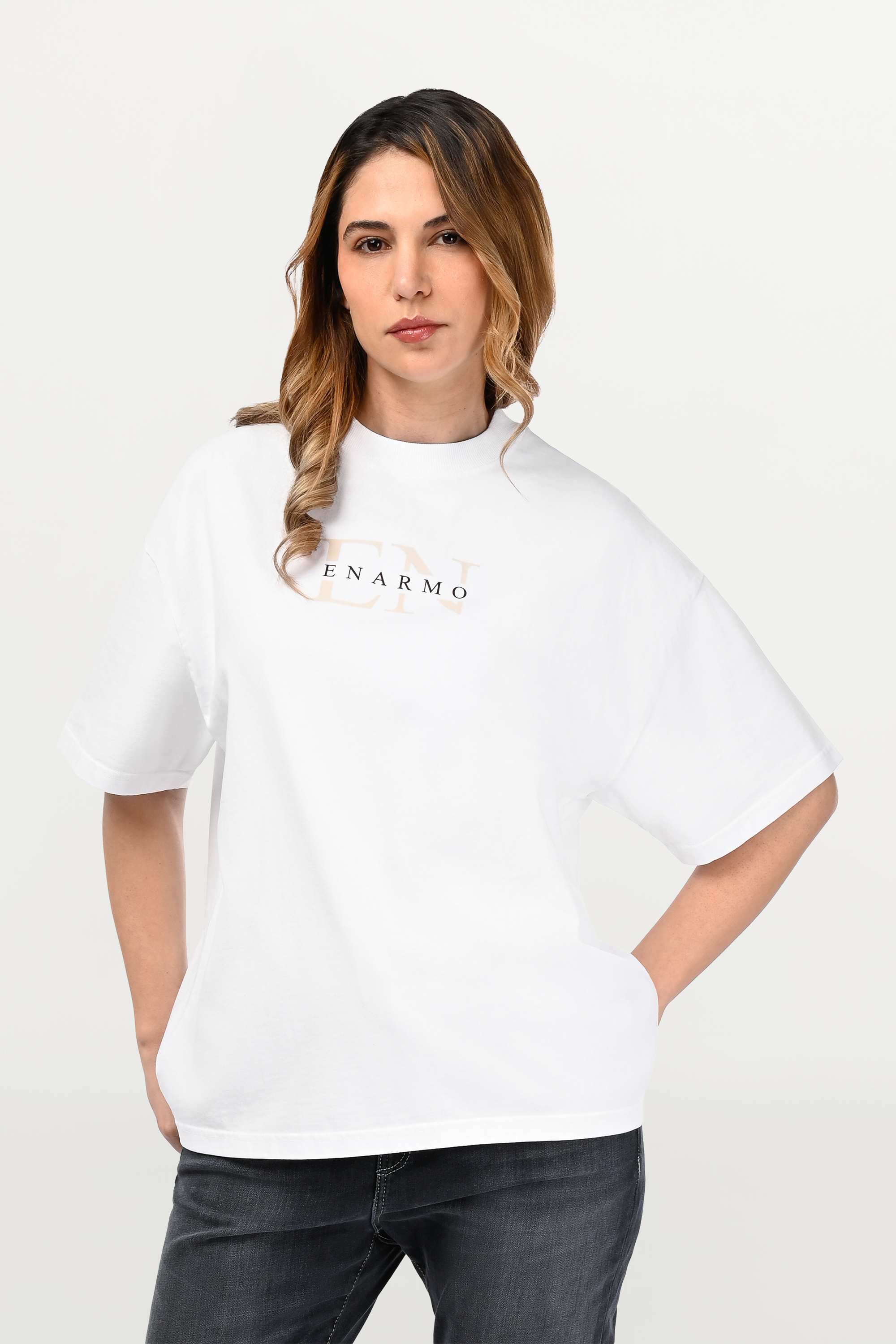 Close-up of white oversized ENARMO T-shirt showing beige EN monogram with black logo detail on chest, worn by female model