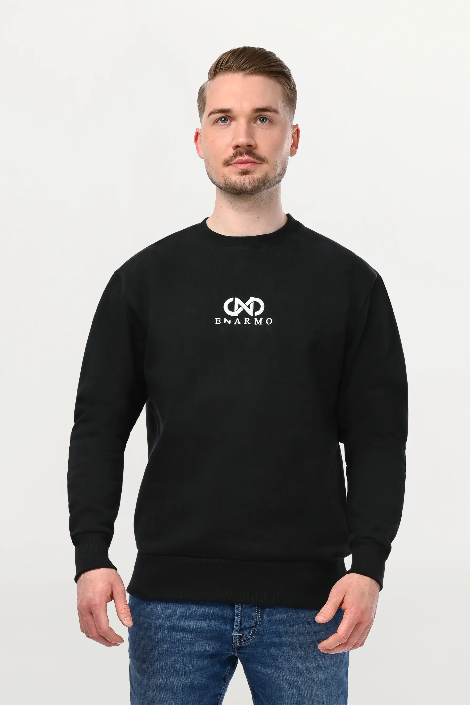 Close-up of male model in black crewneck featuring silver embroidered ENARMO motif, detailed stitching and structured cotton texture.
