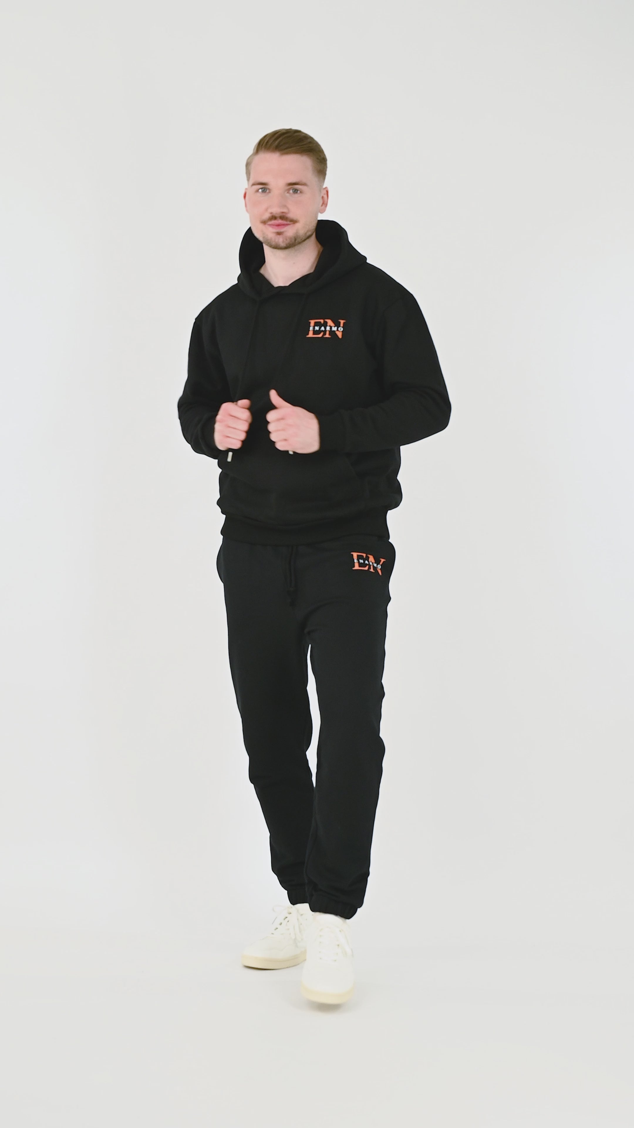 Male model wearing black cotton hoodie with orange and white EN monogram, turning, posing and moving from front, side and back to highlight fit and design from multiple angles.