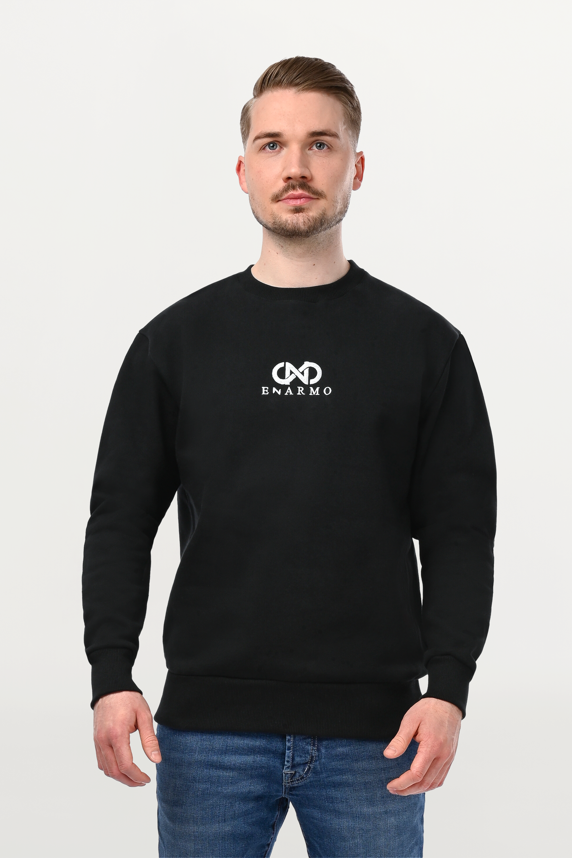 Close-up of male model in black crewneck featuring silver embroidered ENARMO motif, detailed stitching and structured cotton texture.